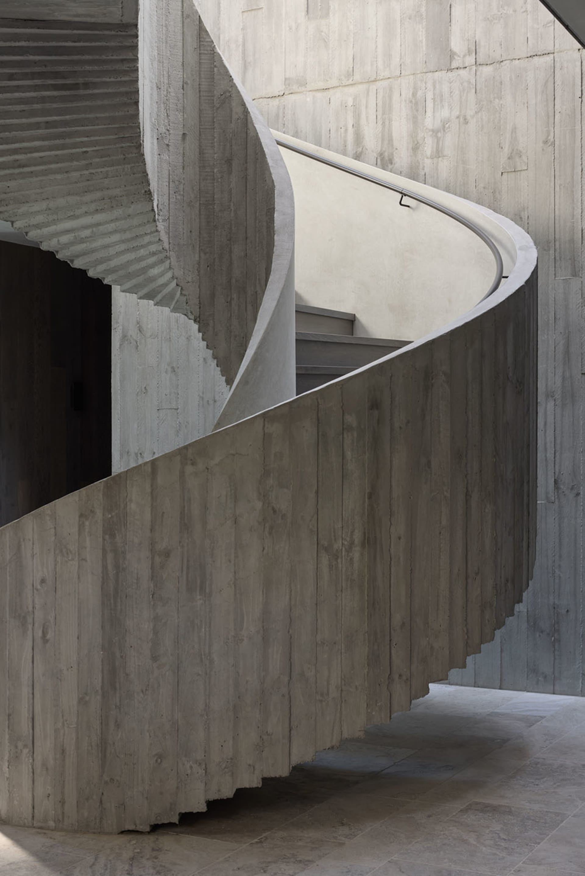 A modern concrete staircase with smooth, curved steps and a handrail.