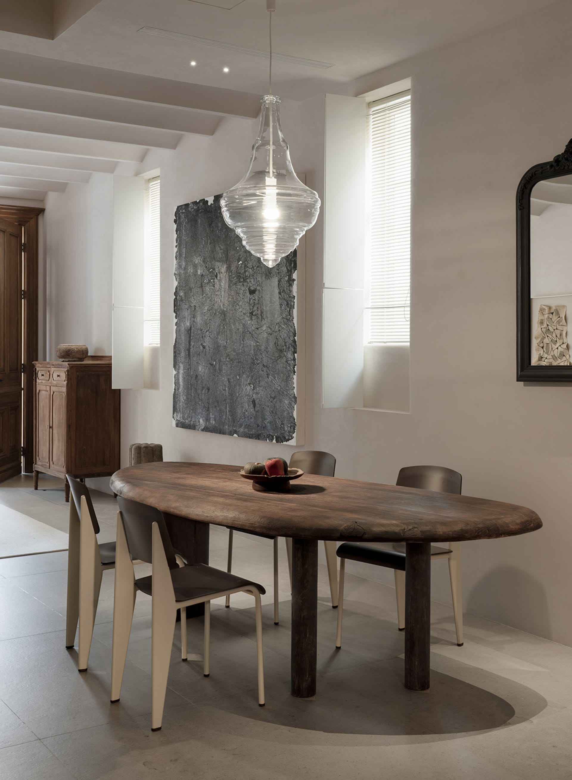 A modern home interior featuring a wooden dining table with minimalist chairs and a large pendant light hanging overhead.
