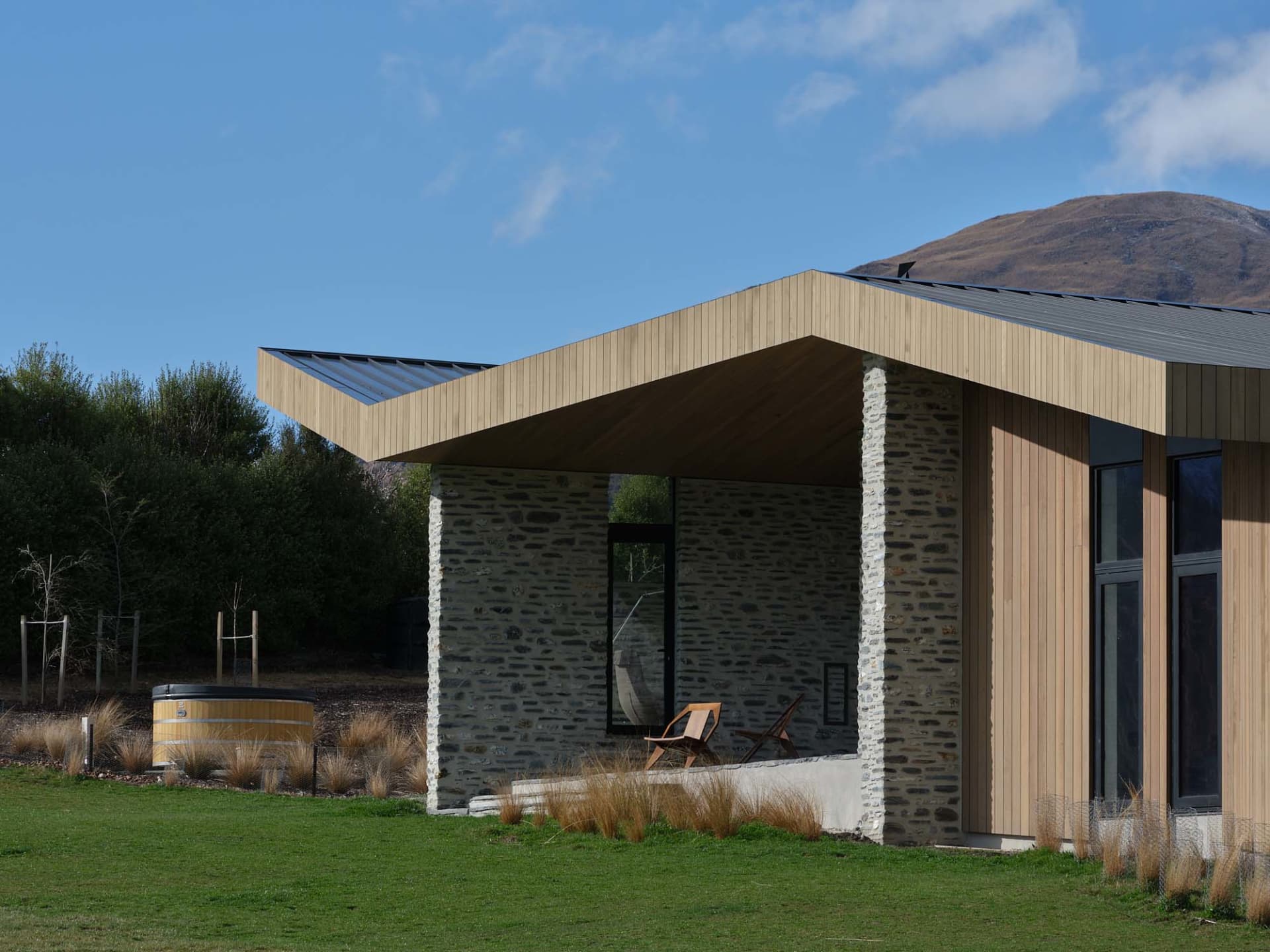Modern residential exterior with stone and concrete materials and a wooden roof.