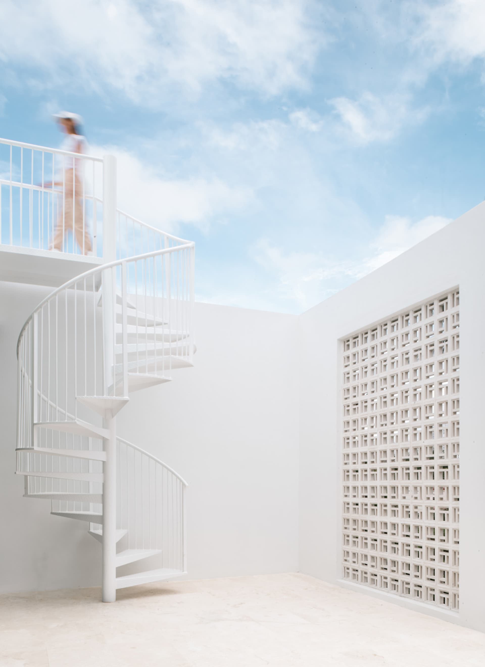 A white architectural space with a spiral staircase and a person walking on the upper floor.