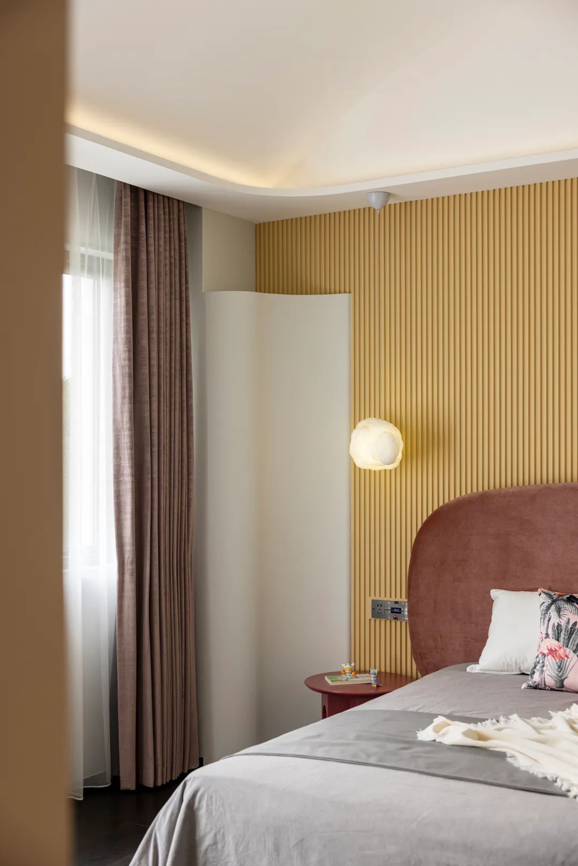 Modern bedroom featuring a velvet headboard and wooden paneling on the wall with soft lighting and a cozy atmosphere.