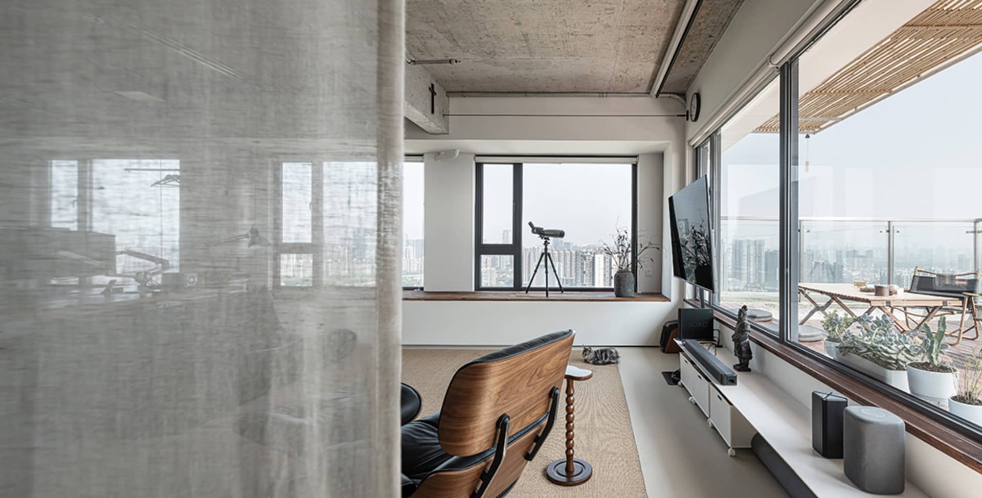 A modern, minimalist living room with concrete finishes, a large window, and a single armchair.