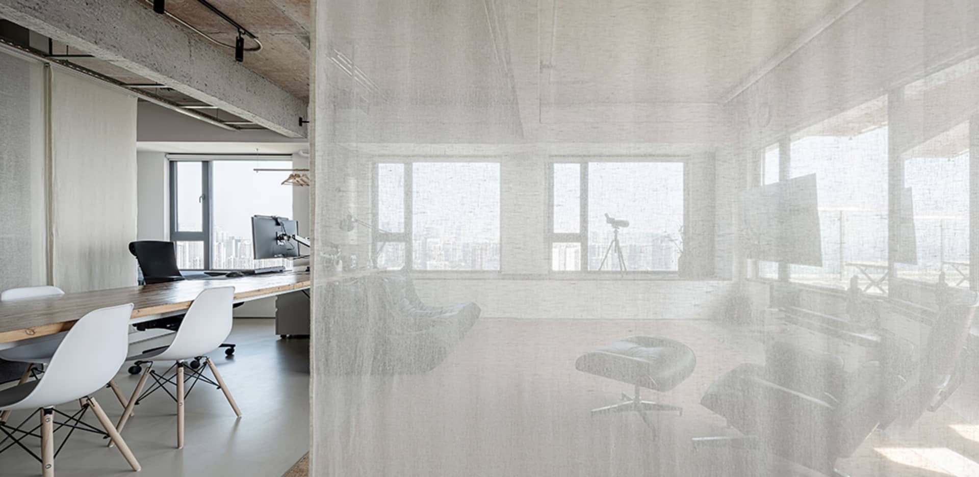 Modern office conference room with concrete walls and floor, large windows, and minimalist furniture.