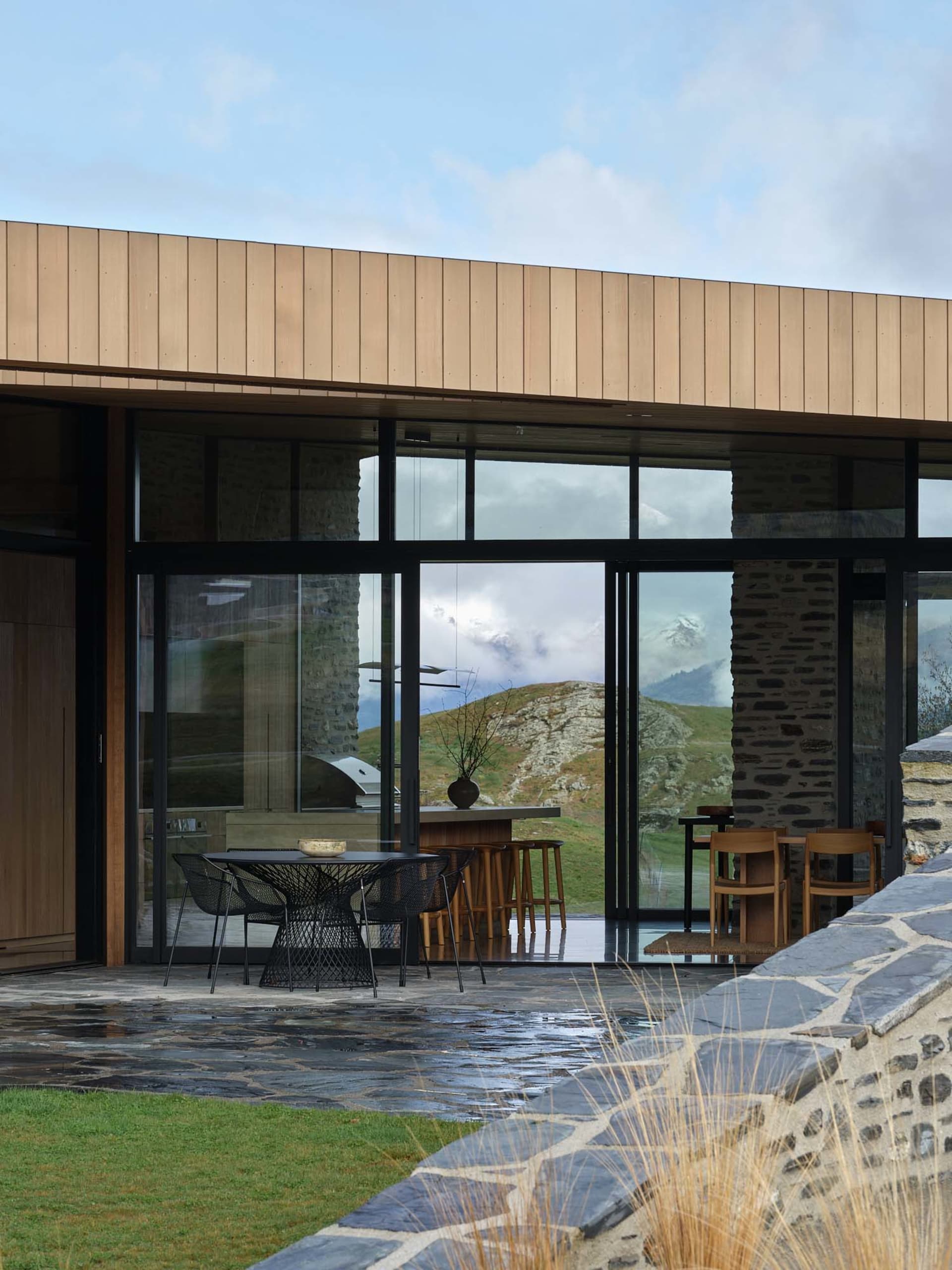 Modern residential interior featuring large glass windows, stone walls, and wooden elements.