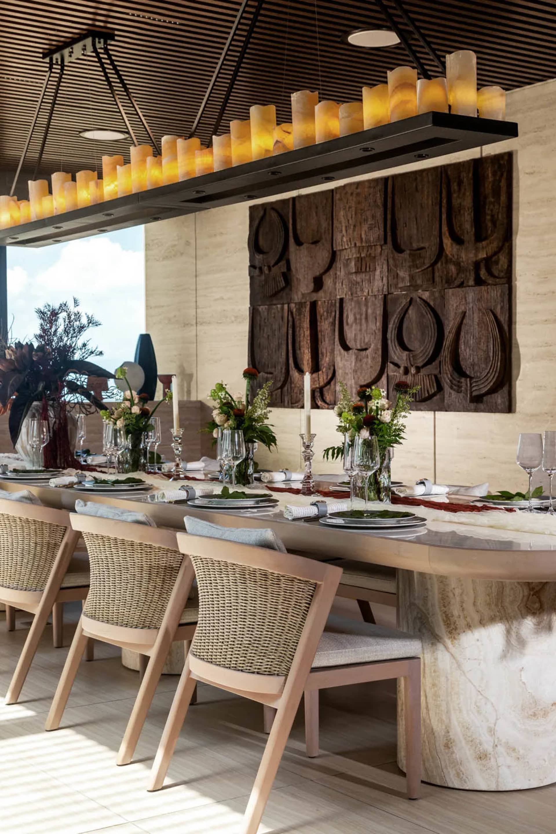A modern dining room features a long stone table adorned with candles and elegant table settings.