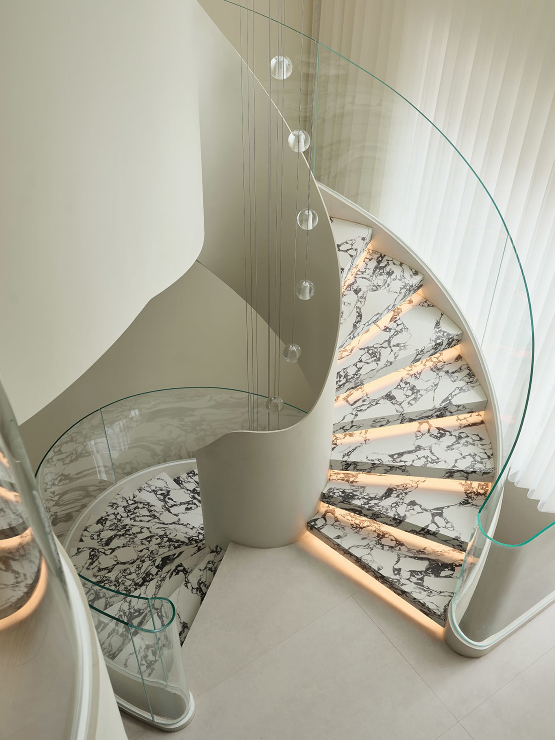 A modern, spiral staircase with marble steps and a glass handrail.