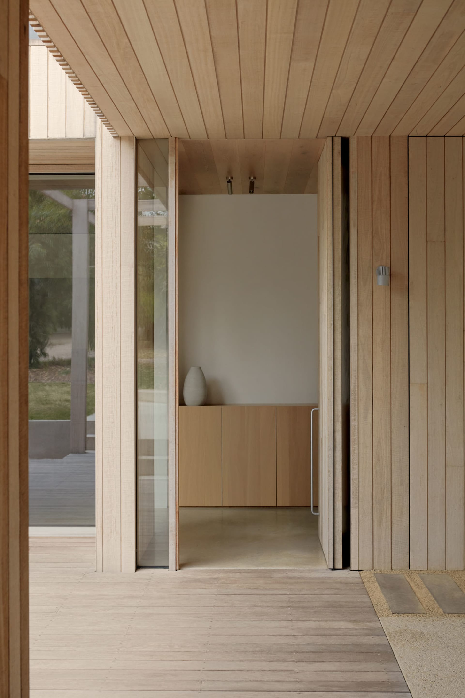 Modern minimalist entryway with wooden walls and large glass window.
