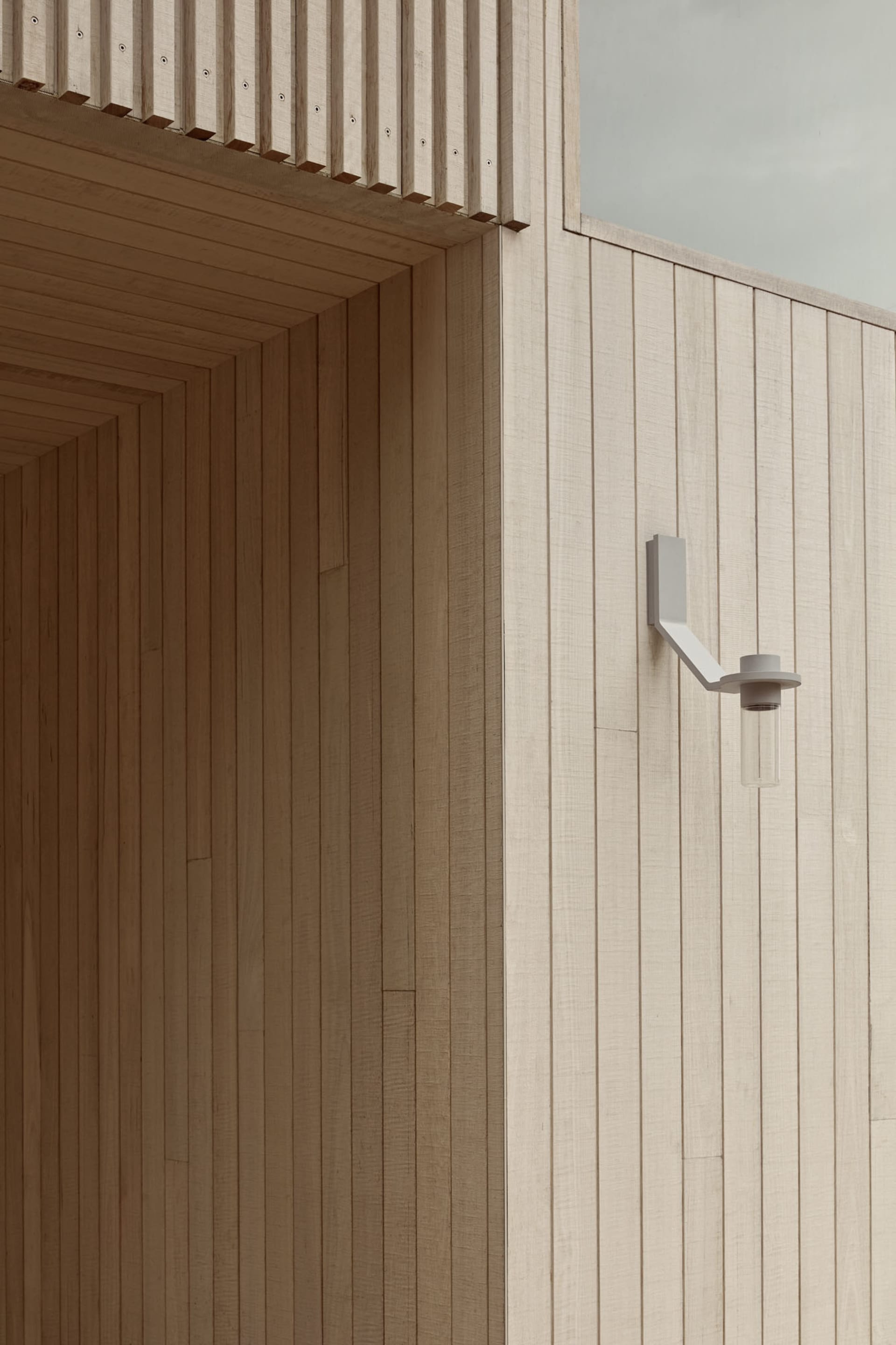 Modern architectural design featuring a white wooden exterior with natural wood grain and a white sconce light fixture.