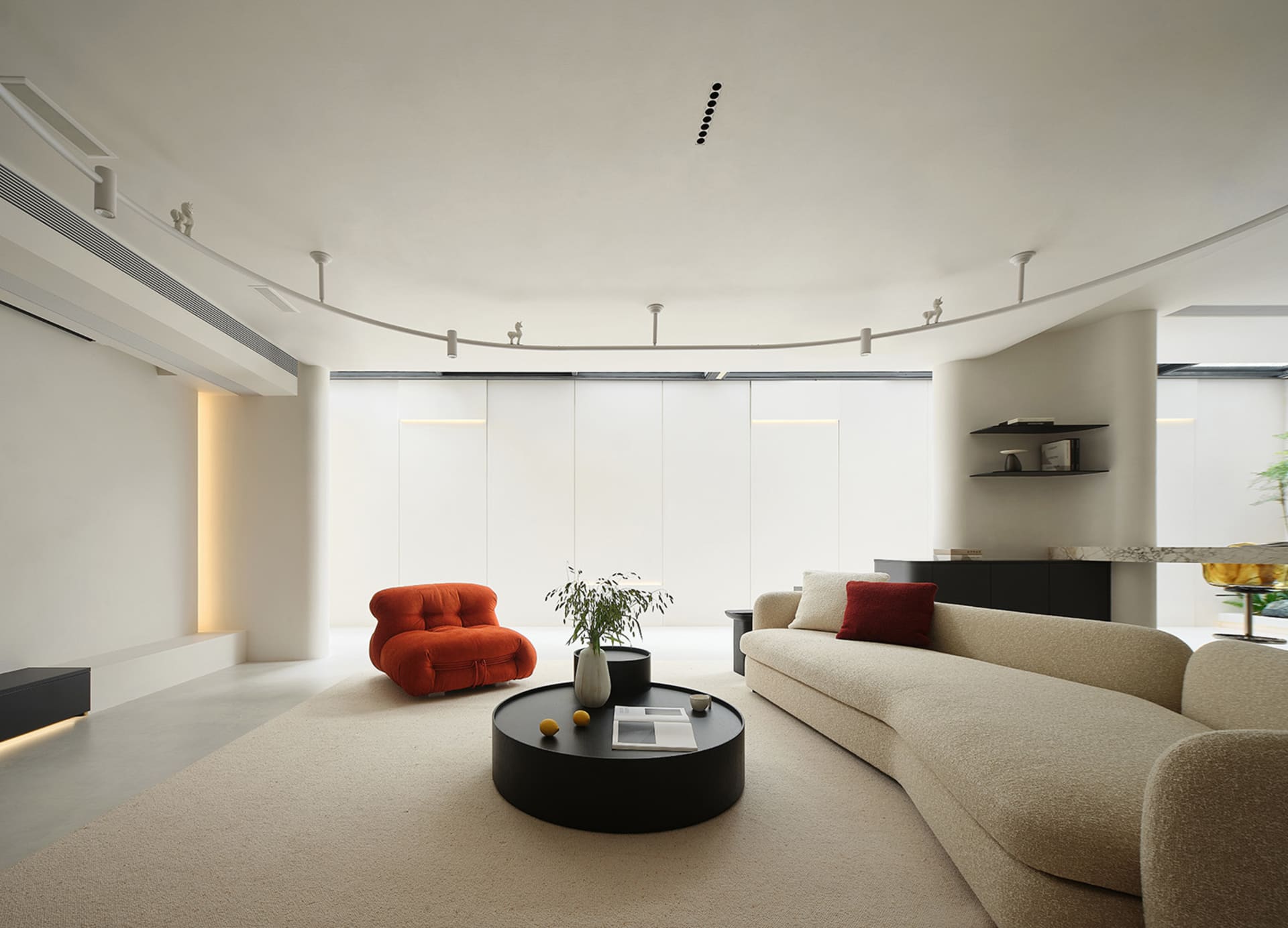A modern minimalist living room with neutral tones, featuring a beige sofa, an orange accent chair, and a black round coffee