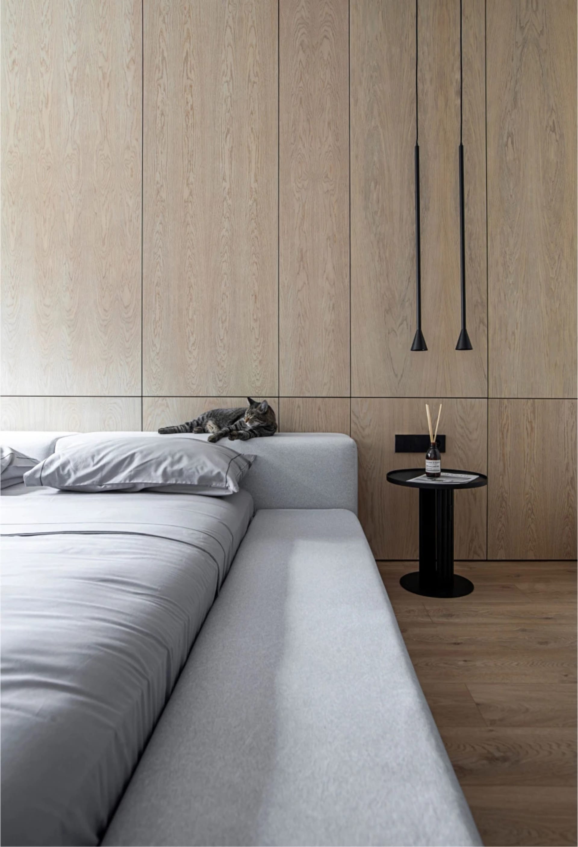 A serene modern bedroom featuring a gray upholstered bed with light wood paneling on the walls and a small side table.