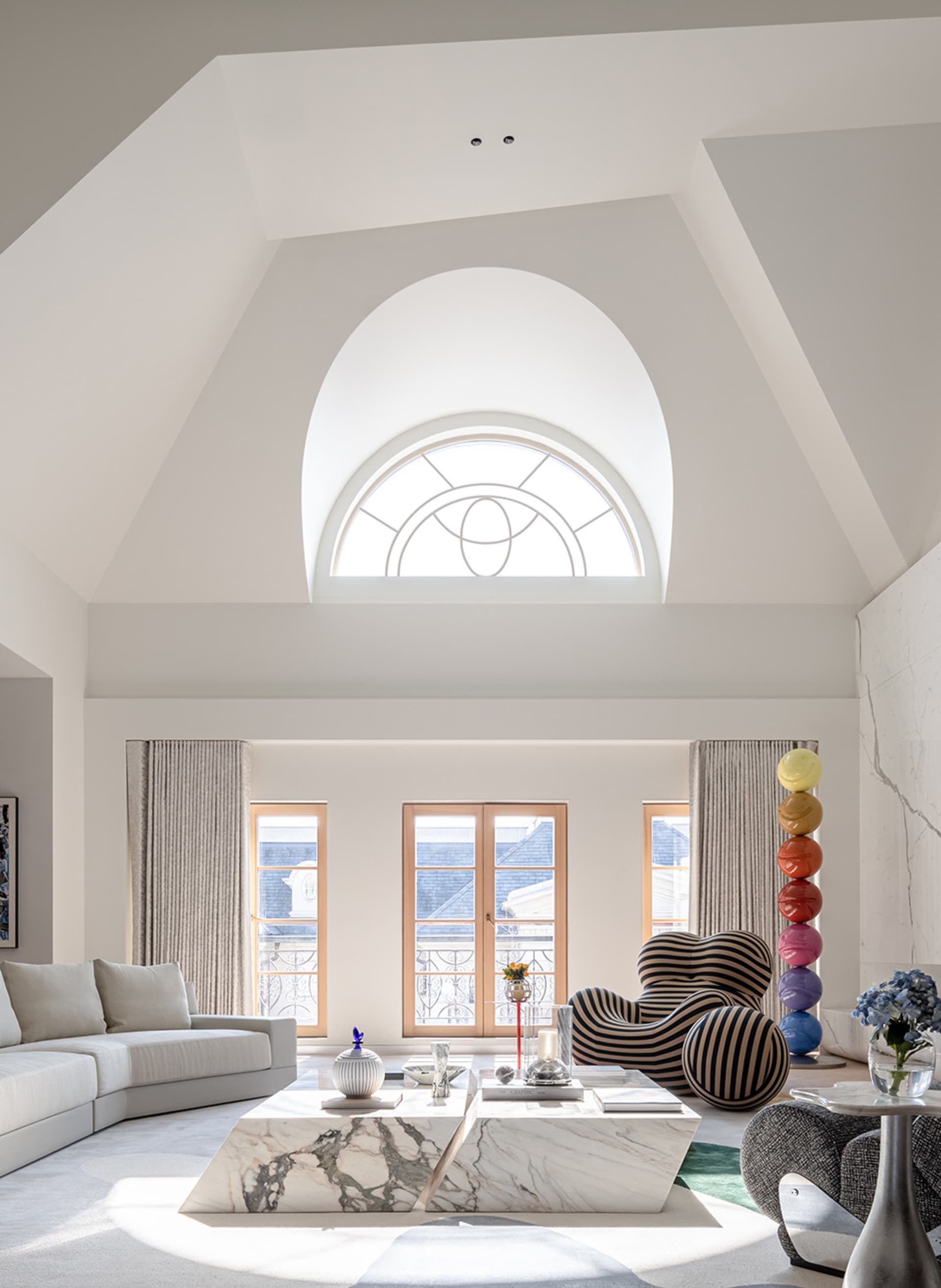 A modern living room with a marble coffee table, striped armchairs, and large arched window.