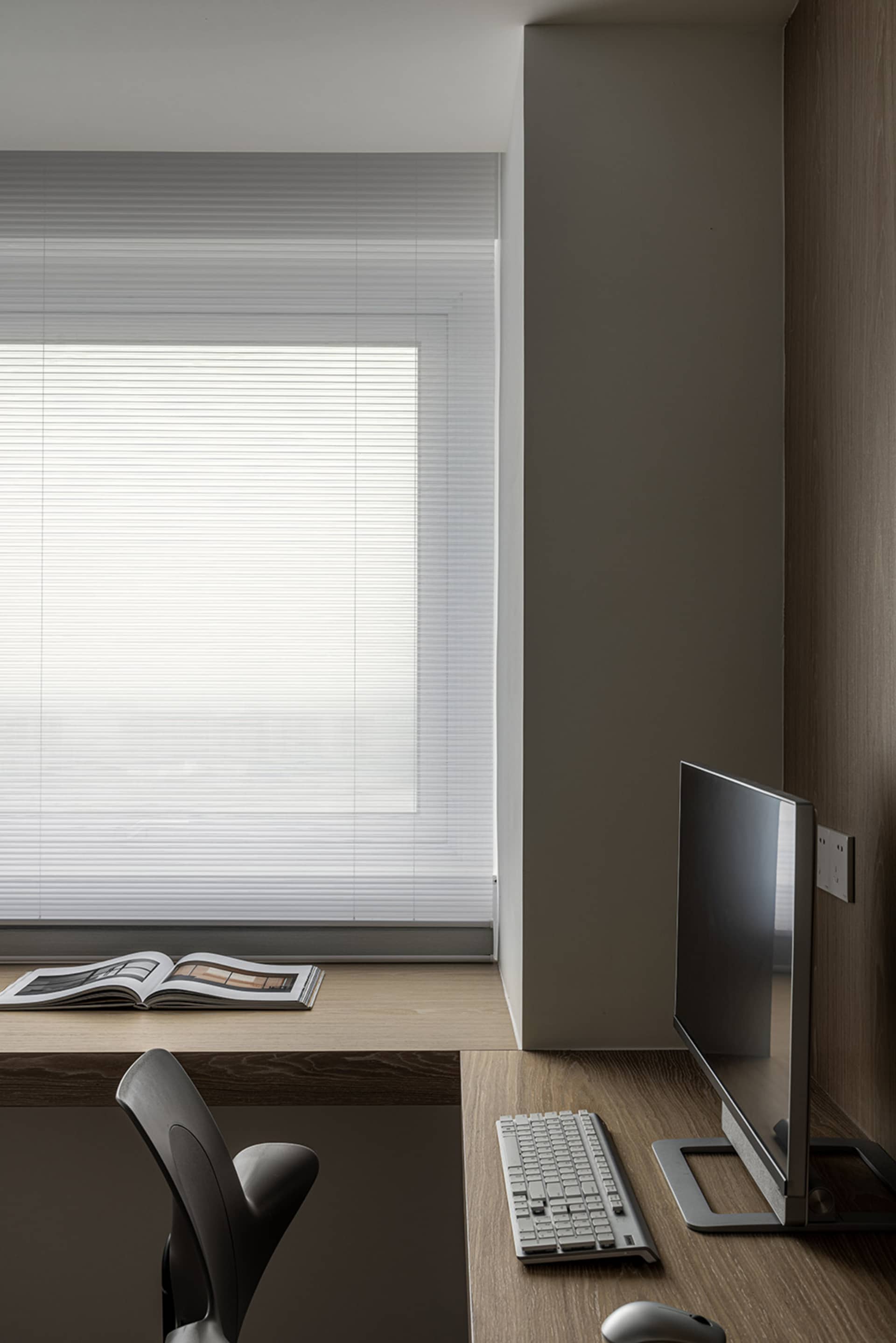 A minimalist home office setup featuring a wooden desk, a sleek computer monitor, a keyboard, and a chair.