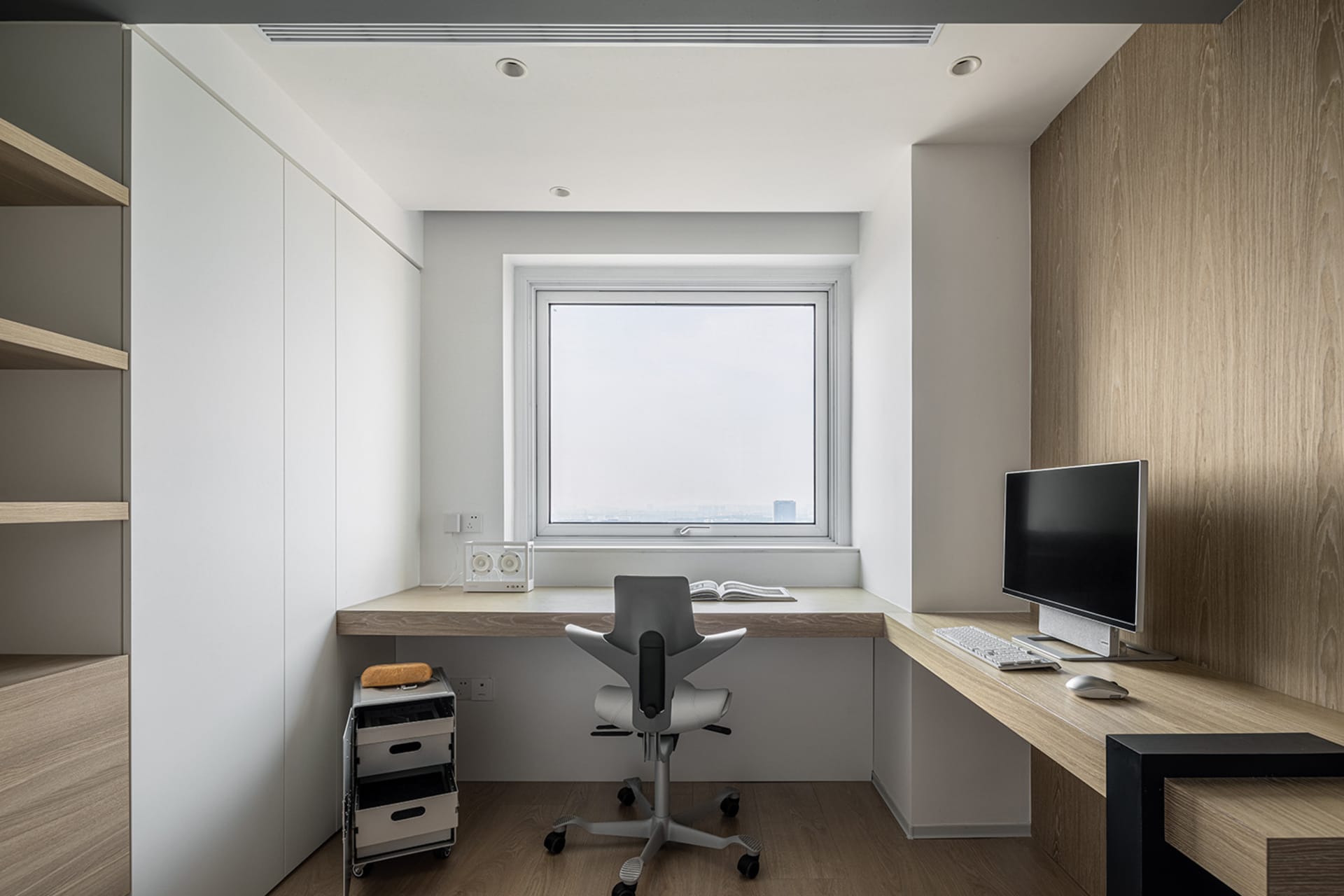 A minimalist home office space featuring a window, desk, chair, and computer setup.