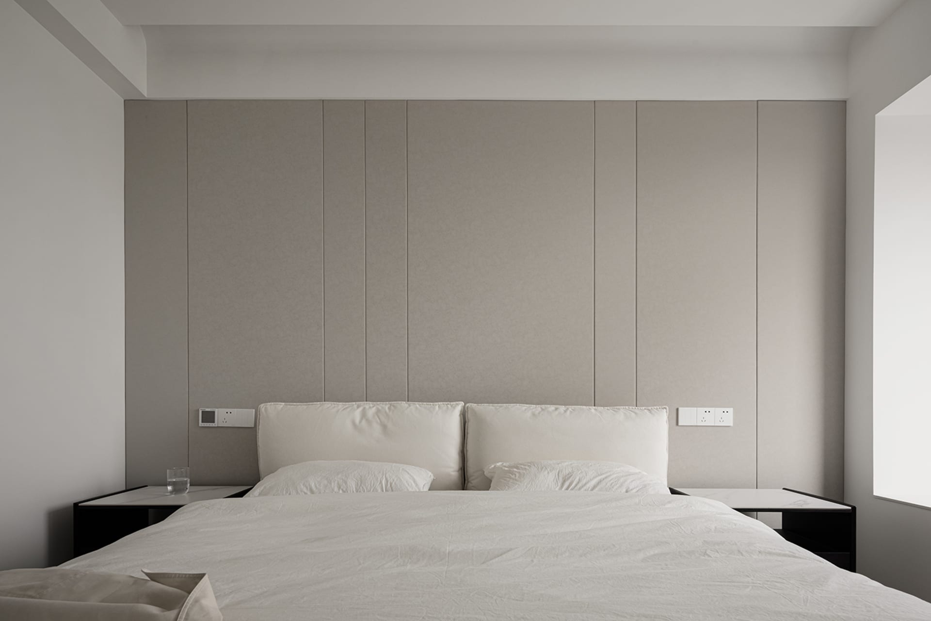 A minimalist bedroom features textured wall panels, a bed with white sheets, and two nightstands.