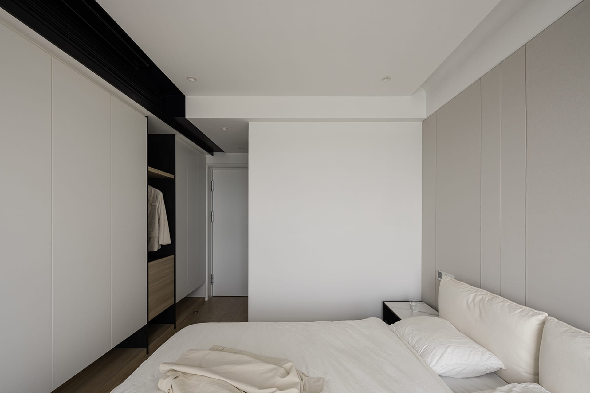 A minimalist bedroom with white and grey walls, a neatly made bed, and hidden storage cabinets.