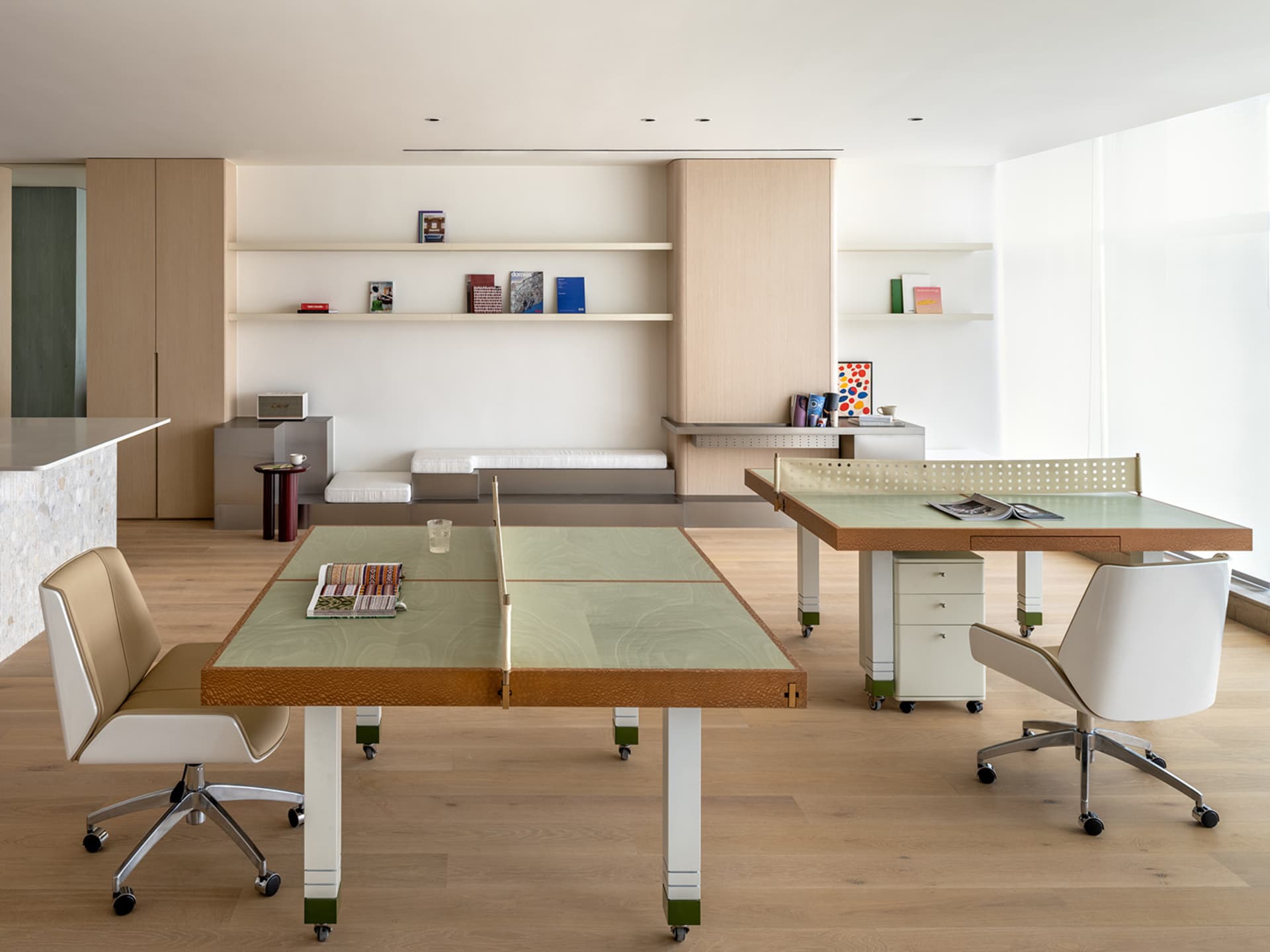 A modern home office space featuring a wooden table and chairs, with books and magazines on shelves in the background.