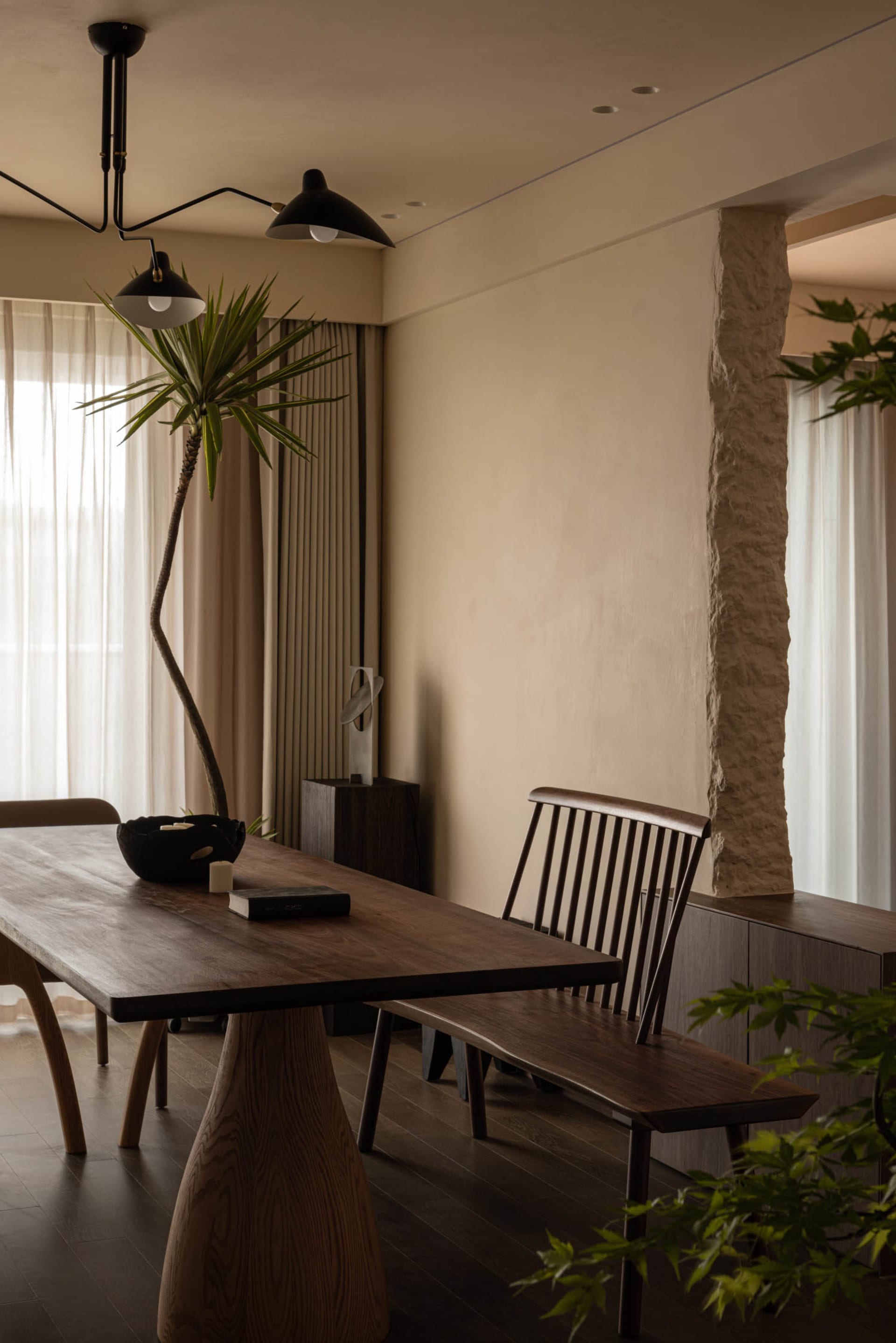 A minimalist dining room with a wooden table, stone pillars, and modern lighting fixtures.