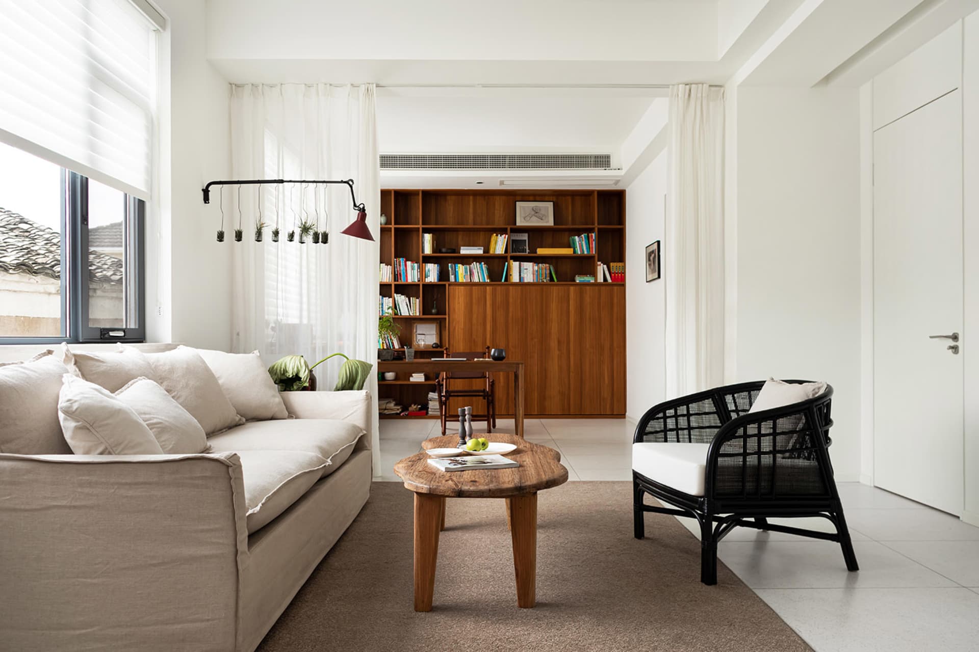 Modern minimalist living room featuring a white couch, wooden coffee table, and bookshelf filled with books and decorations.
