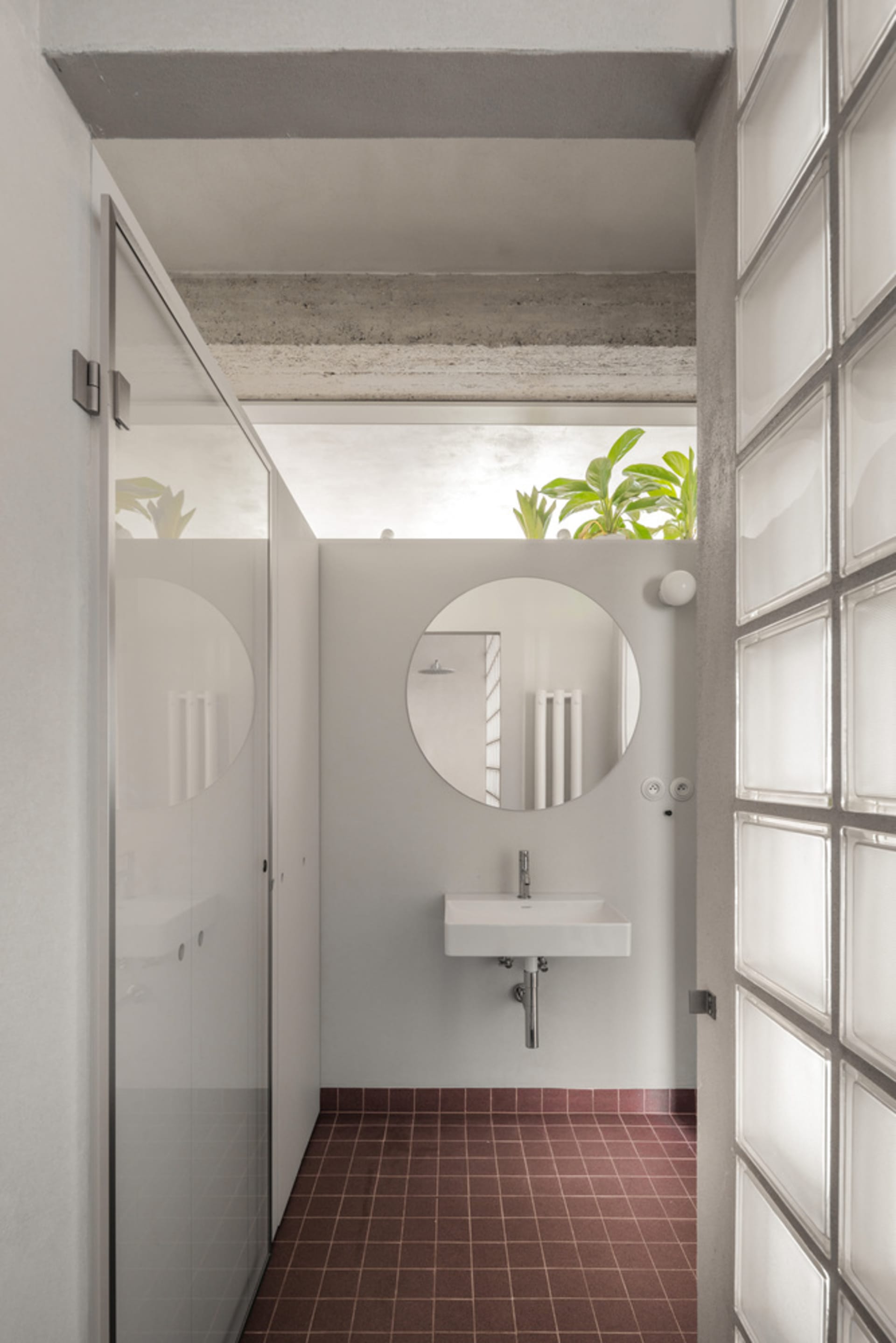 Modern minimalist bathroom featuring a glass shower enclosure, concrete floor, and a circular mirror above a wall-mounted sin