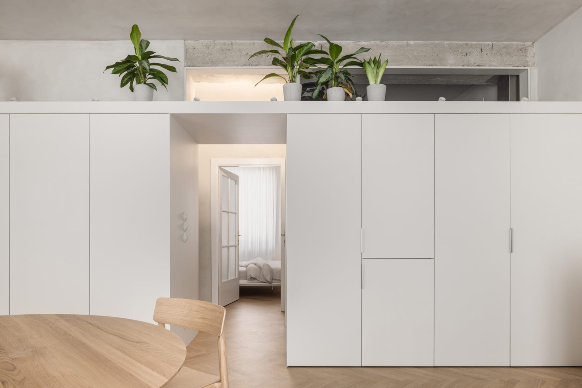 Modern minimalist apartment featuring white concrete walls, white oak floors, and simple white furniture.