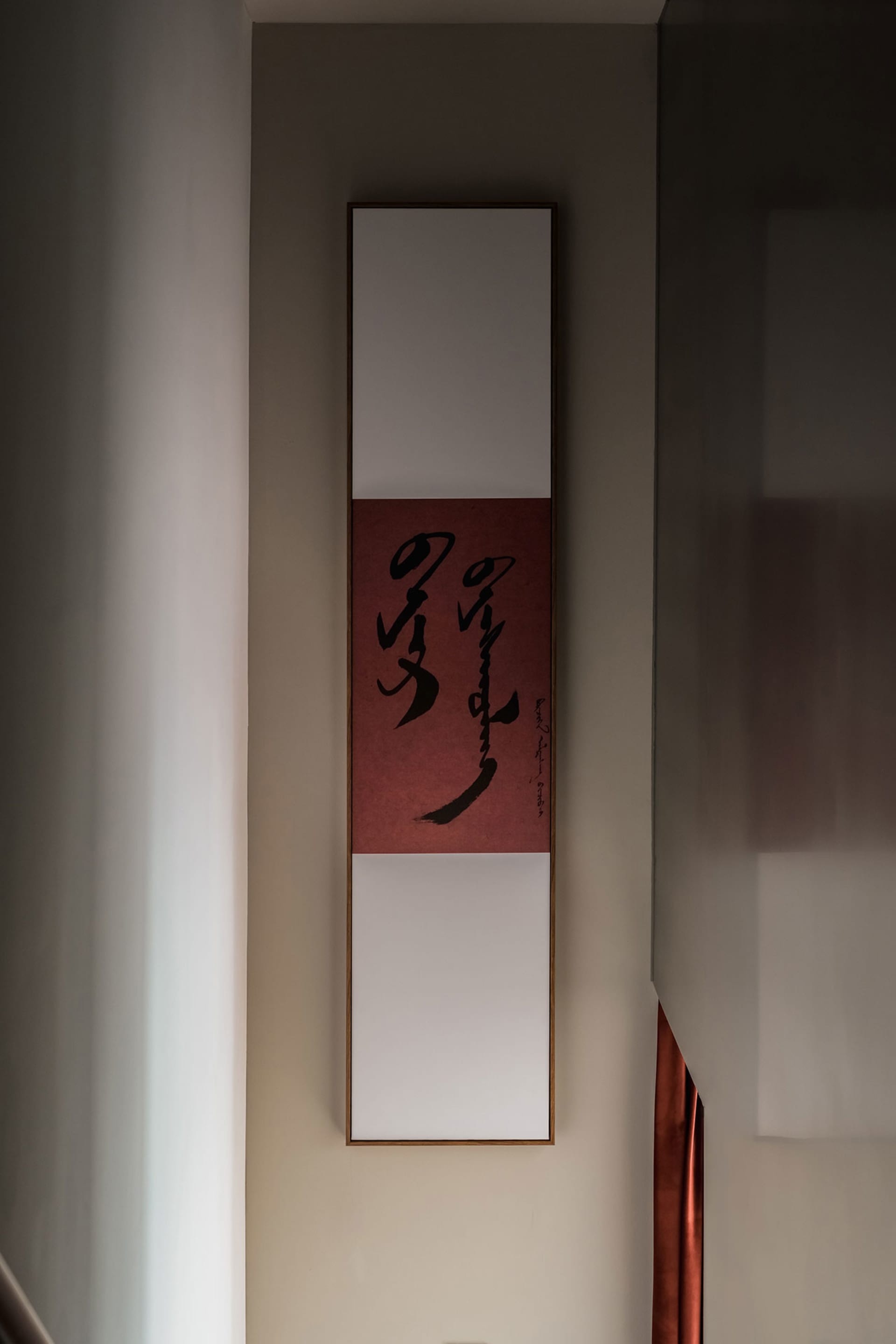 一幅現代風格的書法卷軸,紅底黑字,懸掛在淺色牆面上。
