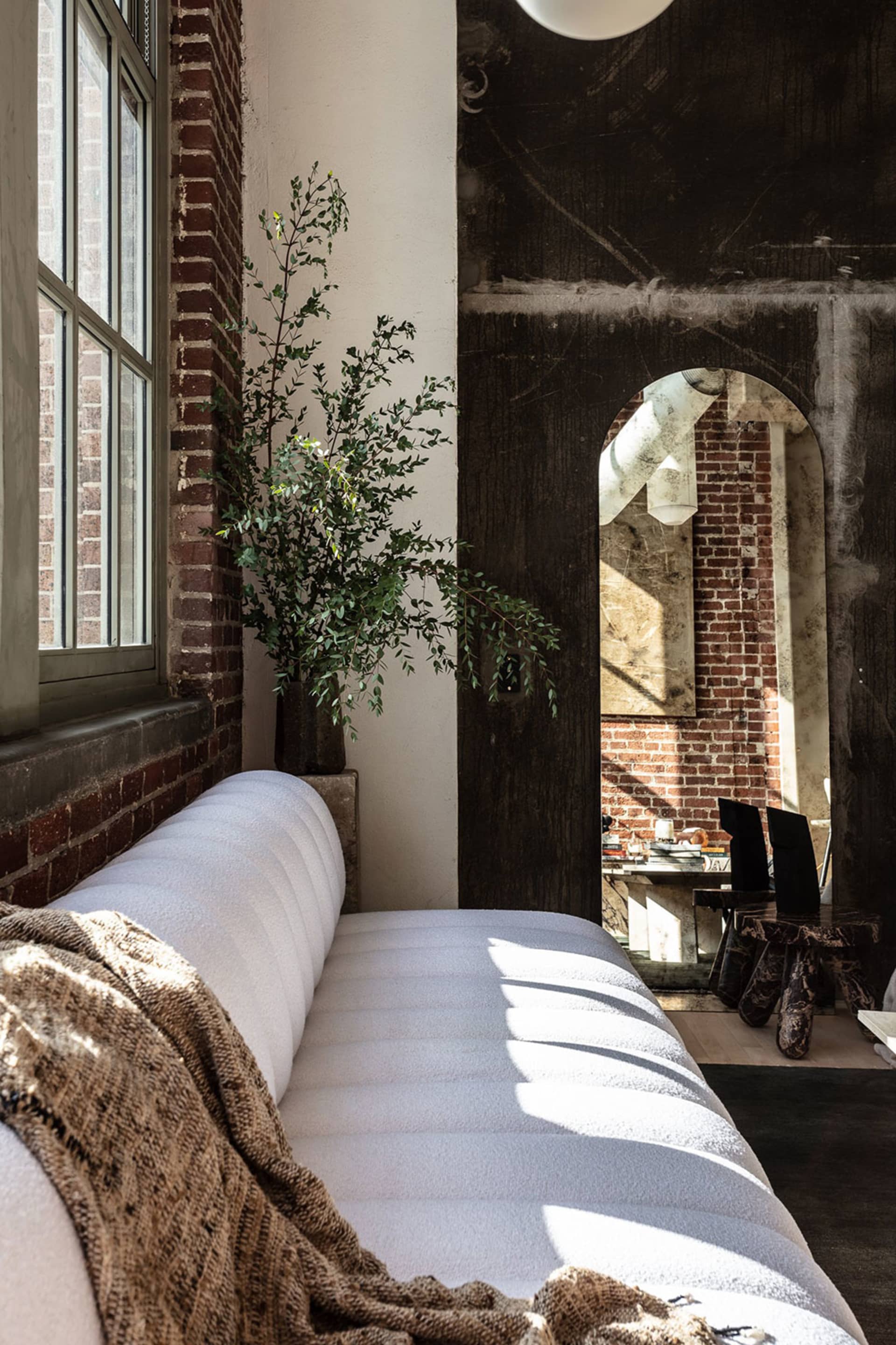 A cozy living room featuring a white sofa, a green plant, and brick walls