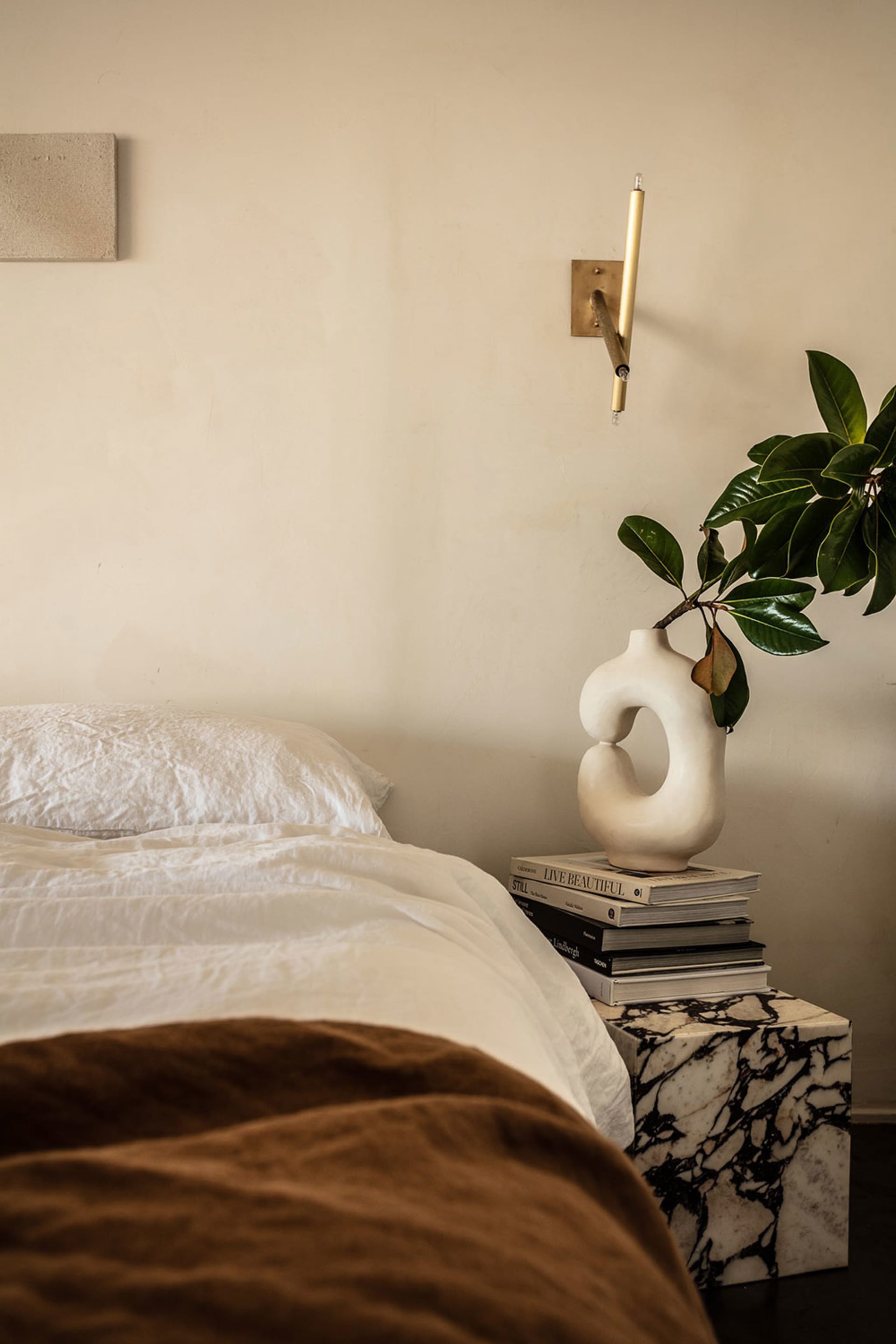 A minimalist bedroom with a white bed and a marble table with a vase and books.