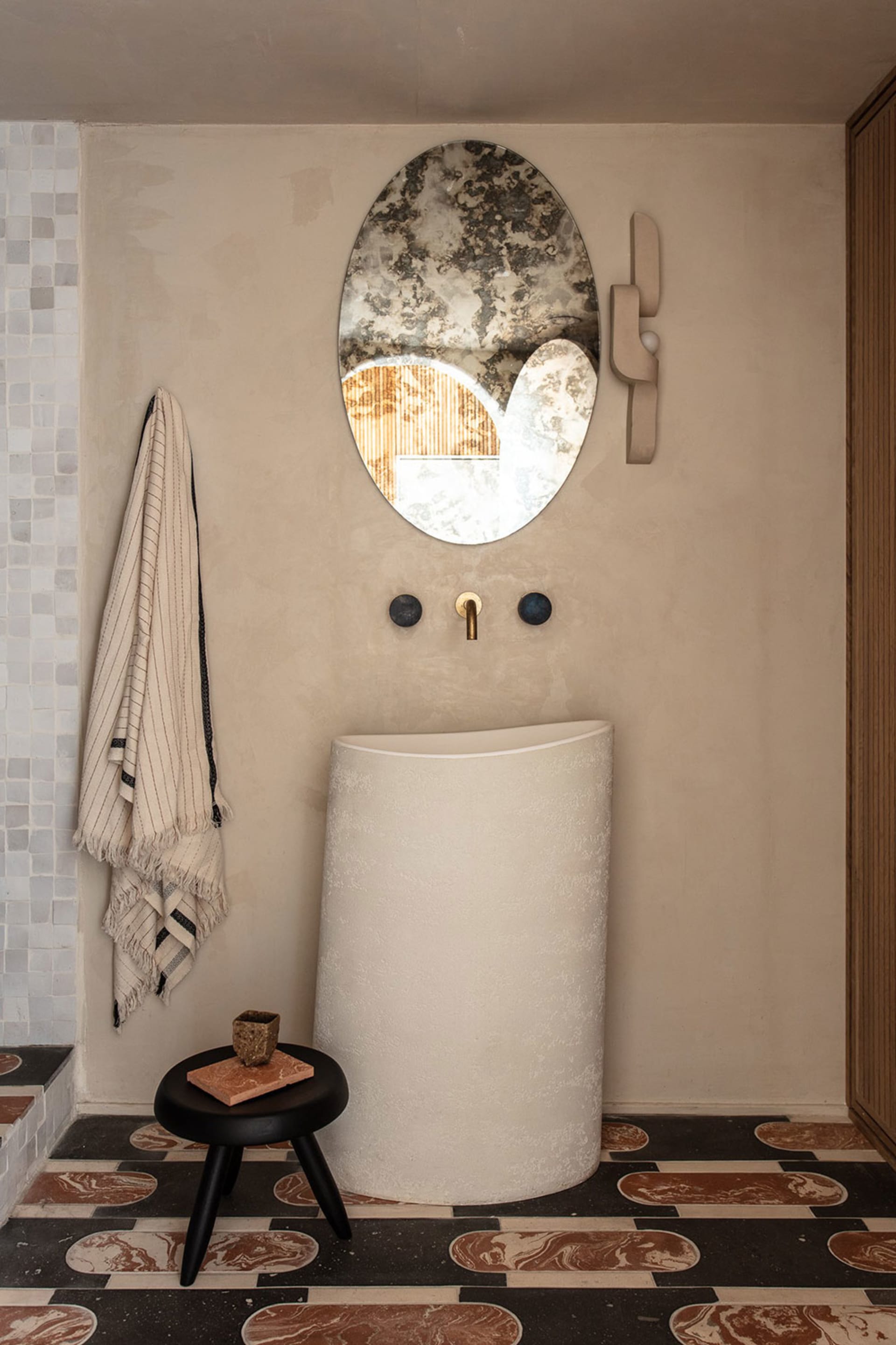 A modern bathroom featuring a concrete sink, round mirror, and patterned floor tiles.
