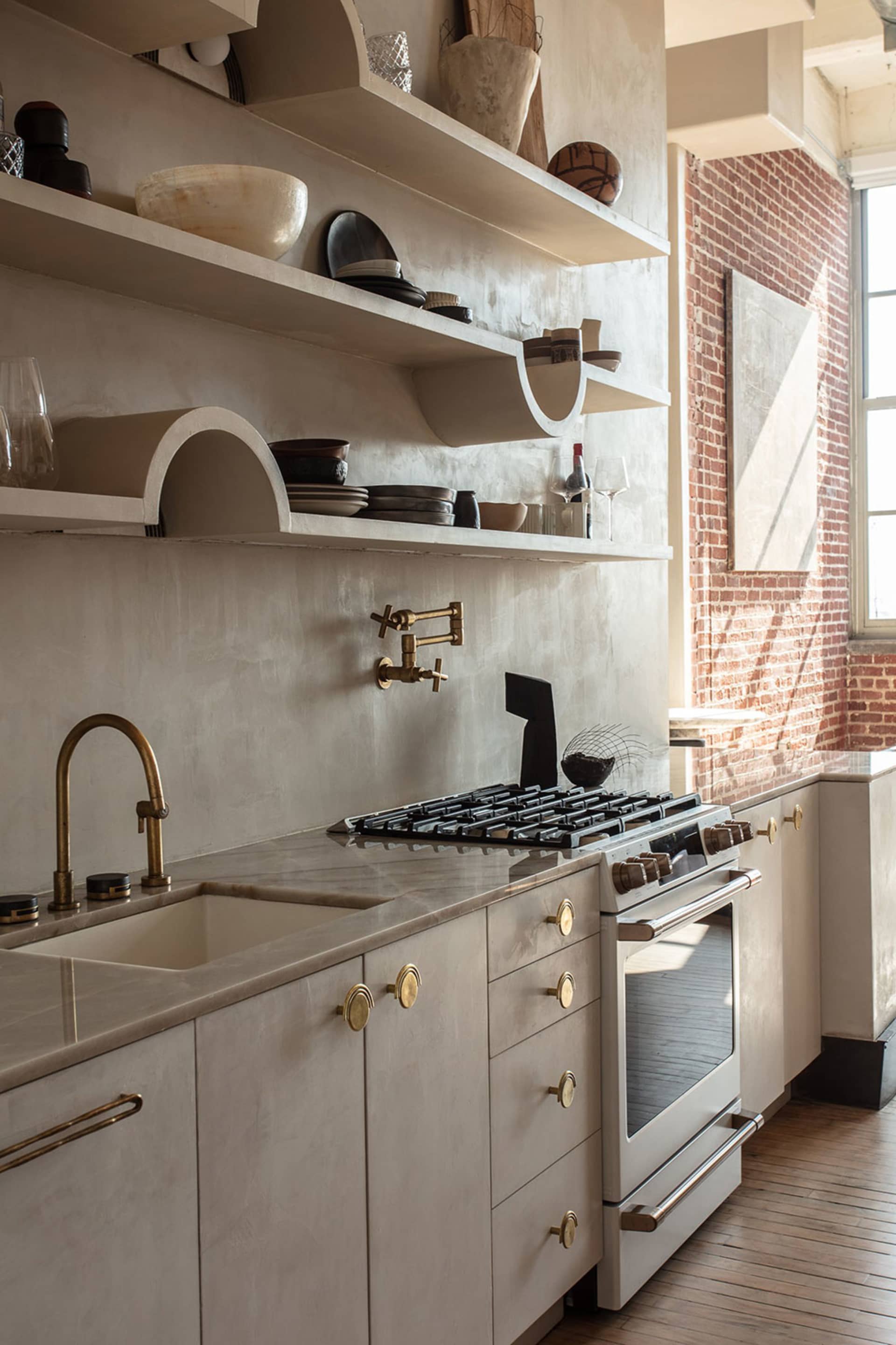 A modern kitchen with concrete backsplash, brass fixtures, and marble countertops.