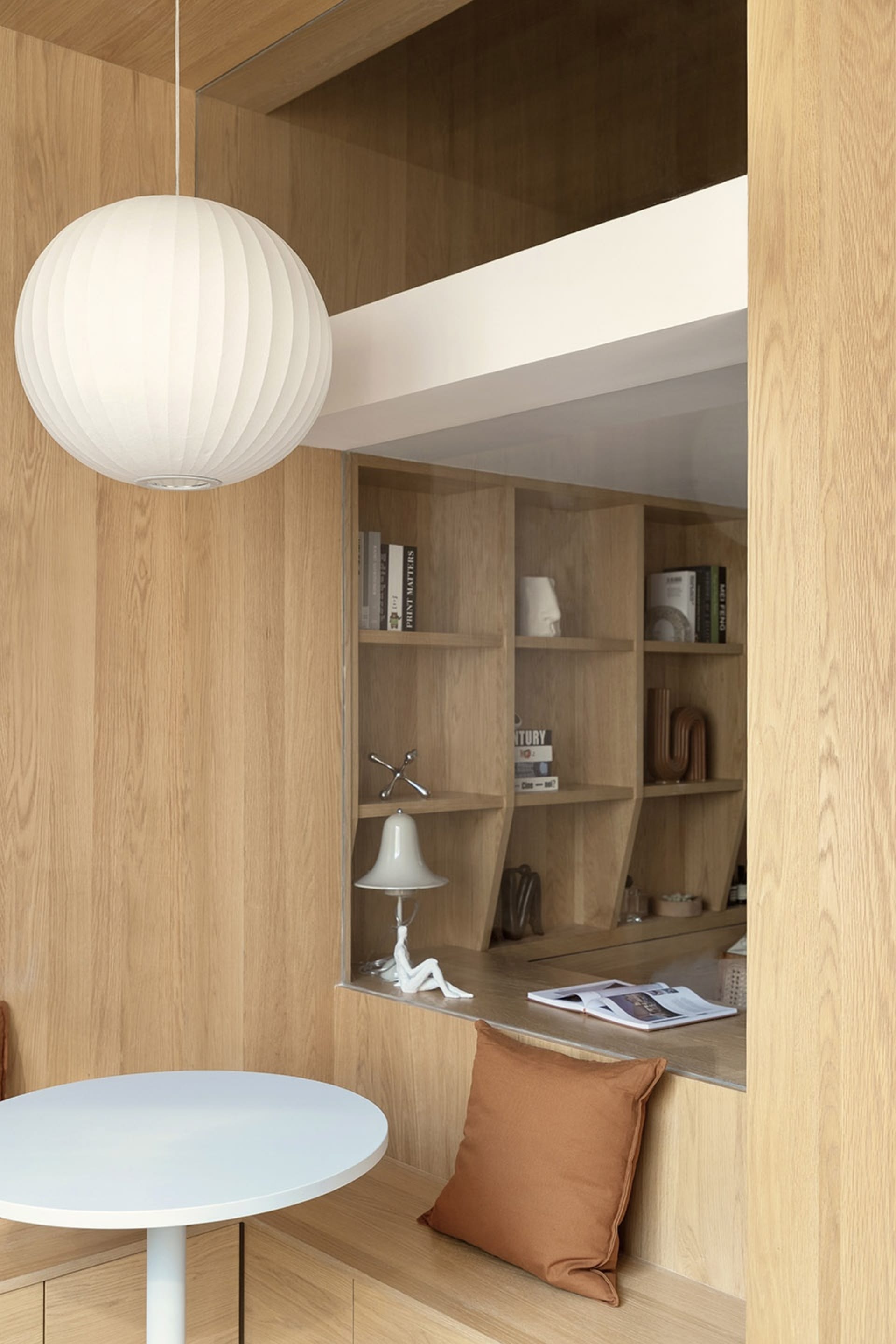 Modern minimalist office space with wooden shelves, a round table, and a white pendant light.