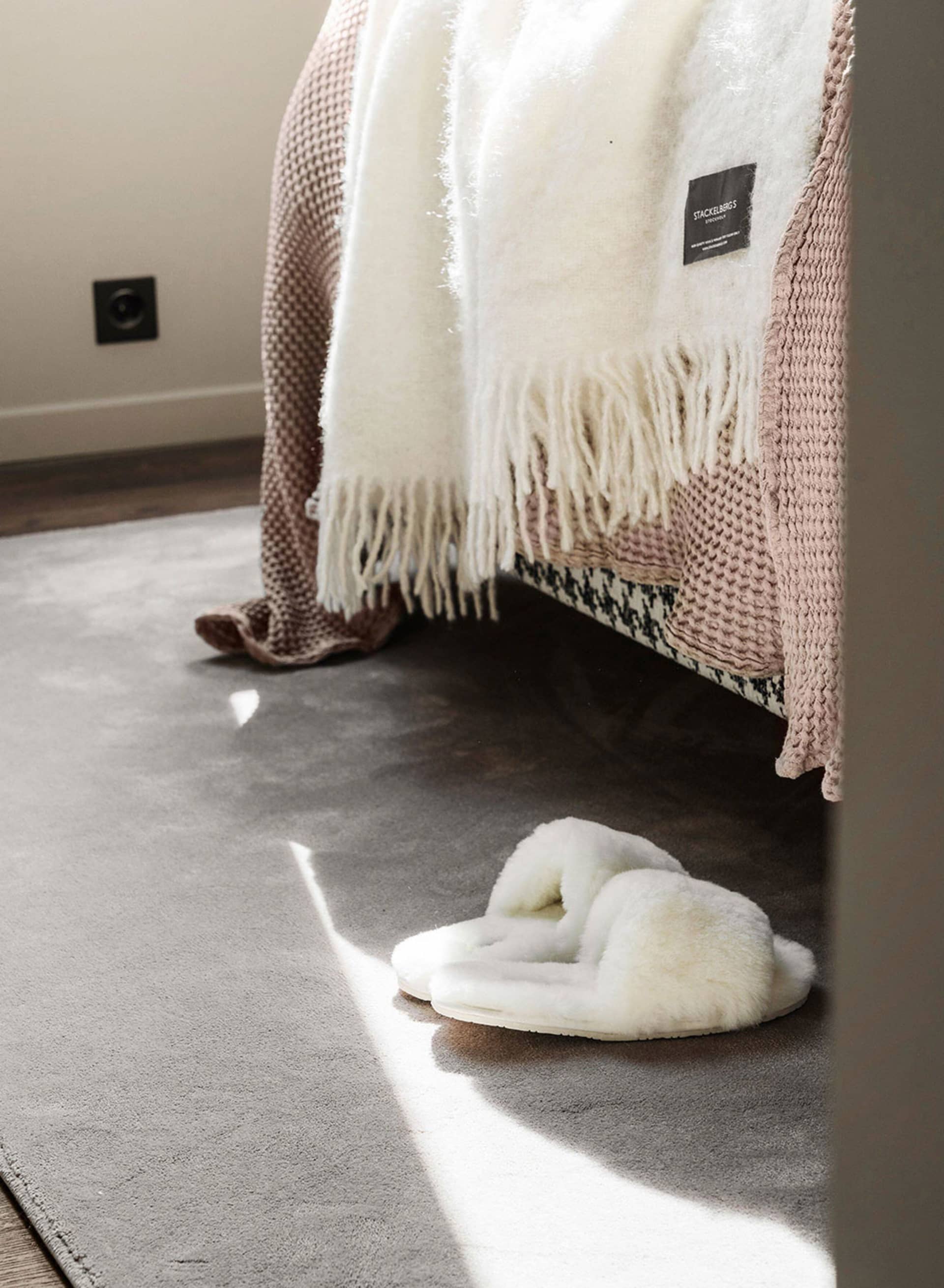 A cozy setting featuring a pair of fluffy white slippers, a textured blanket, and a soft rug in a comfortable home environmen