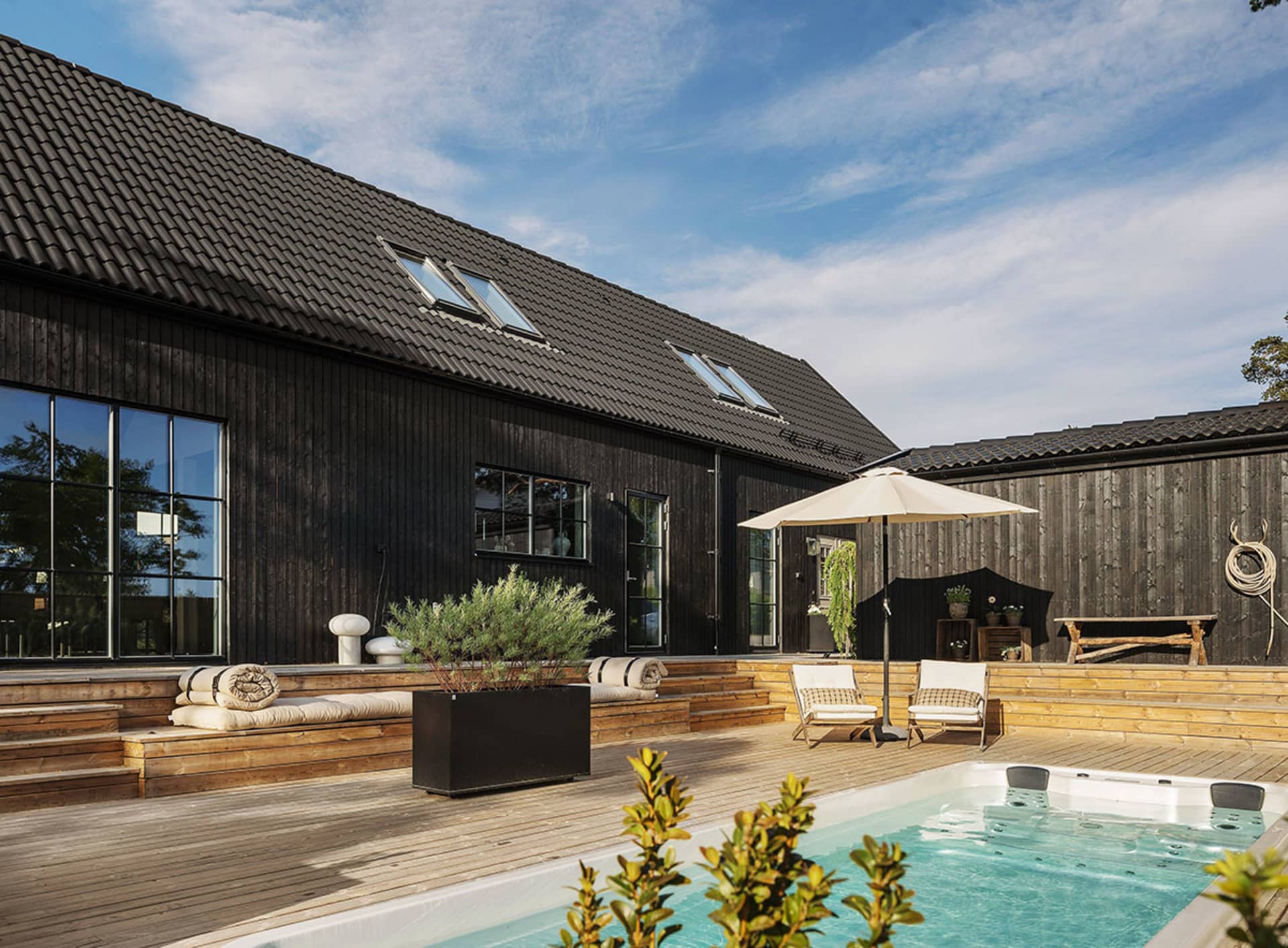 A modern residential exterior features black shiplap siding, a swimming pool, and a hot tub.