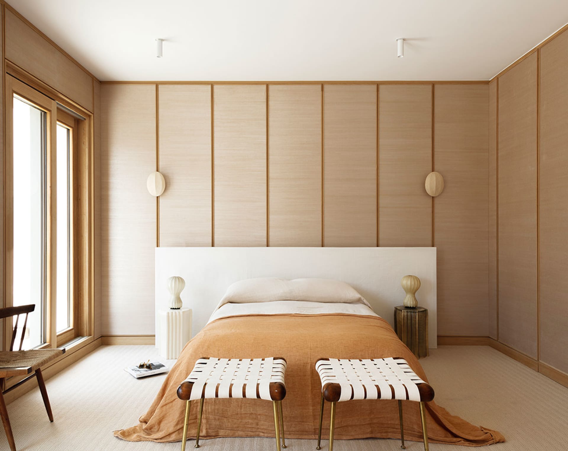 A modern bedroom featuring wooden paneling, a white bed with a wooden headboard, and beige bedding.