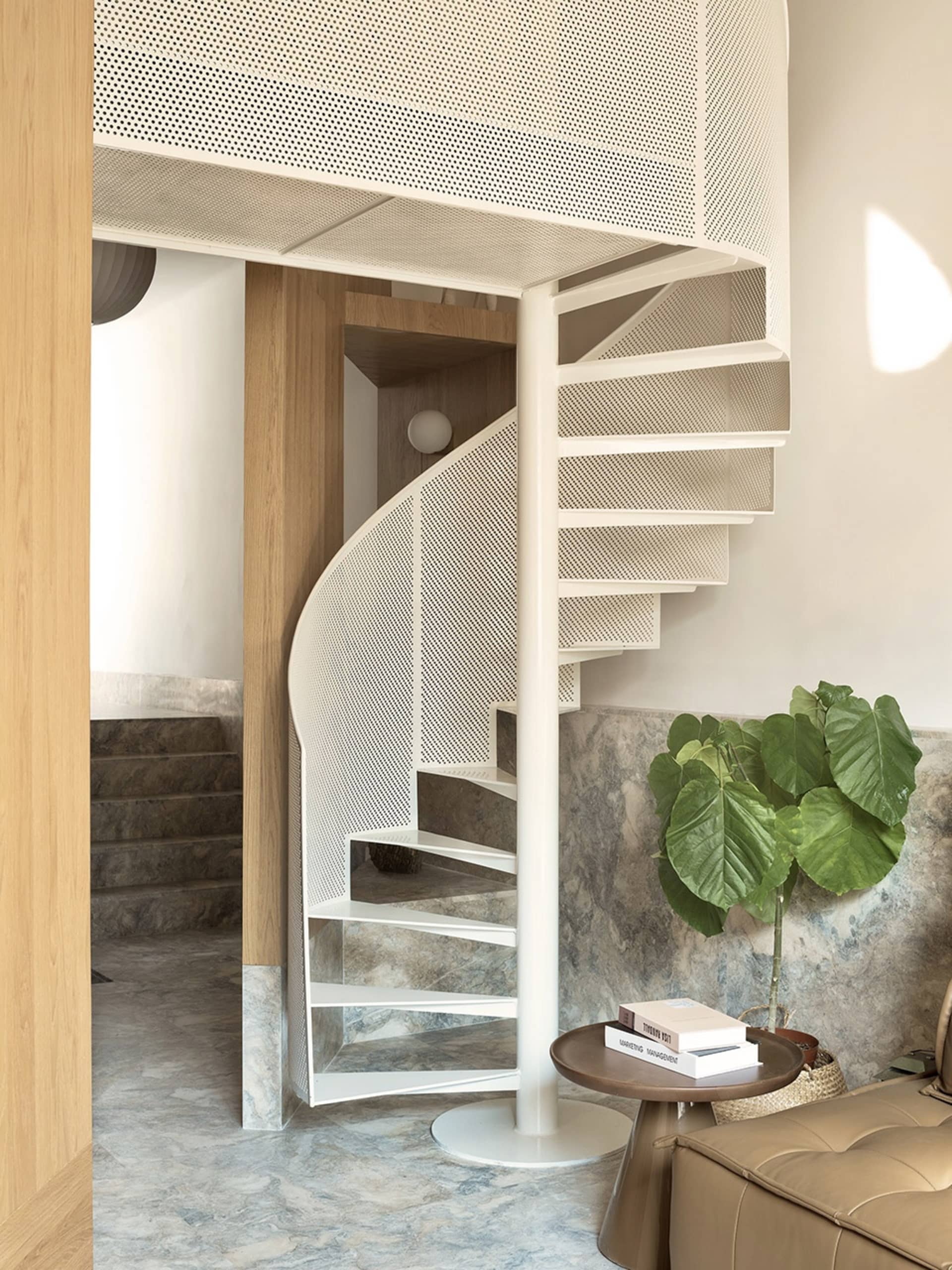 A modern minimalist staircase with white metal and marble steps, featuring a perforated metal railing and a small round table