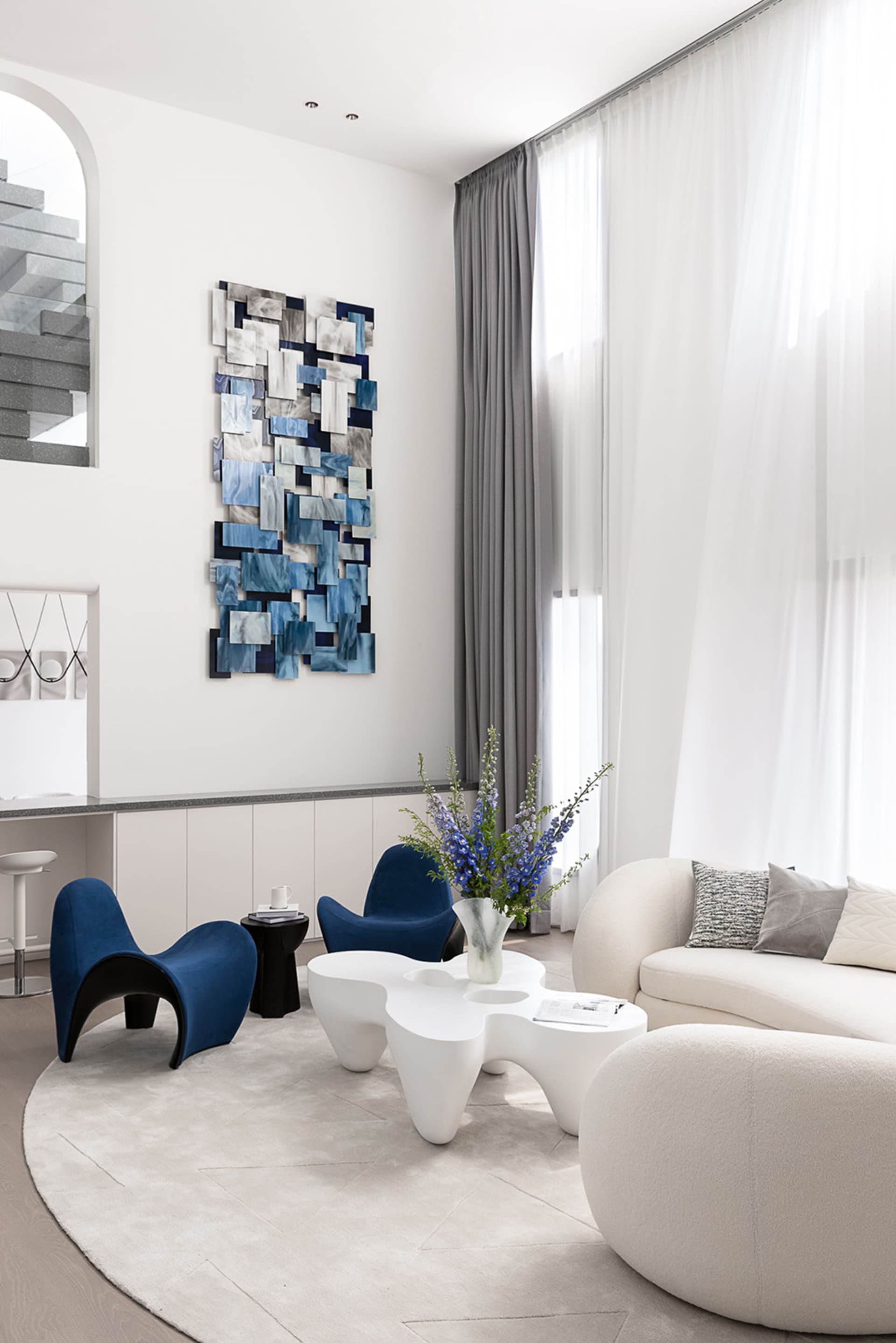 A modern living room featuring abstract art on the wall, a white sofa, blue armchairs, and a round rug.