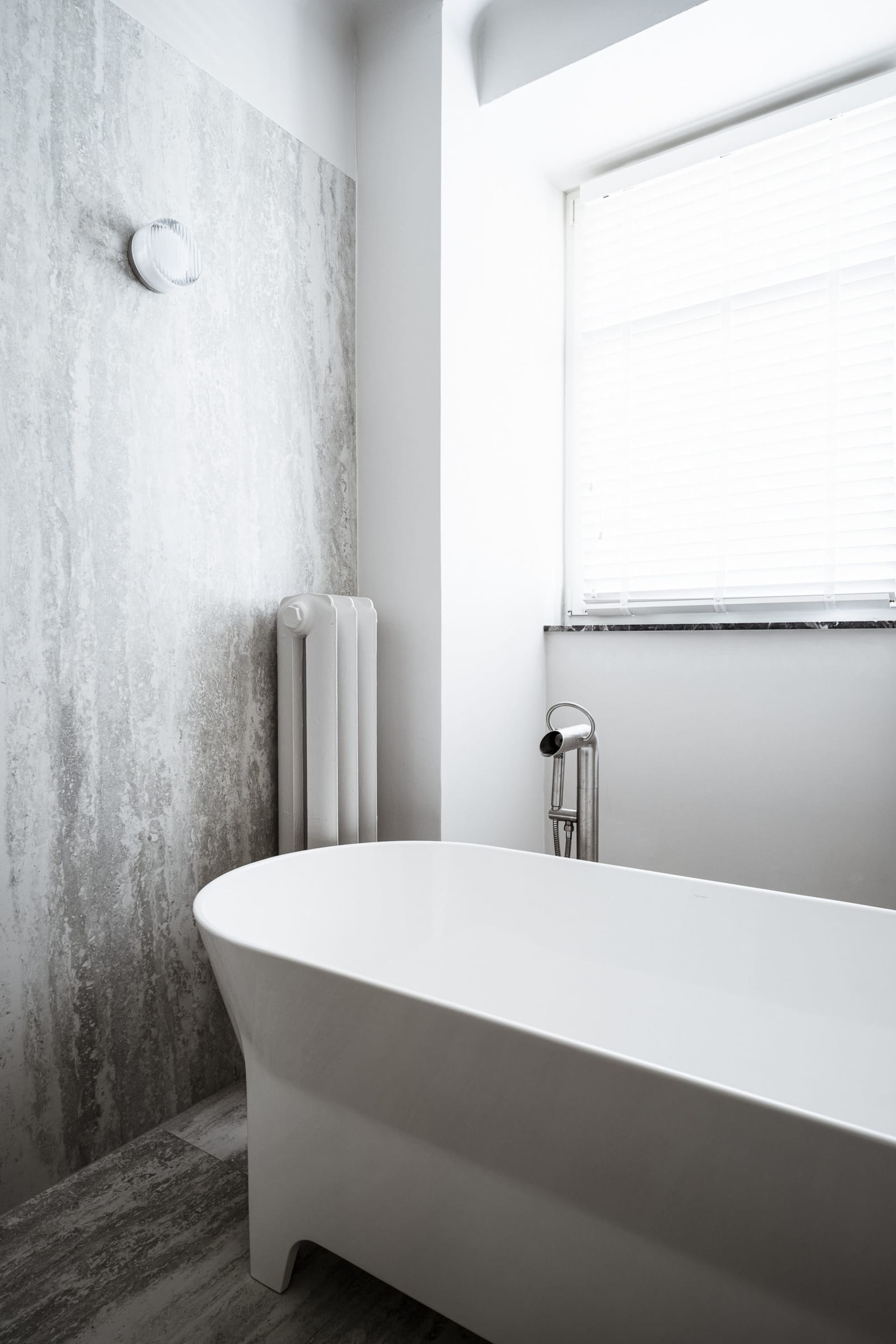 Minimalist bathroom with concrete walls and a white freestanding bathtub.
