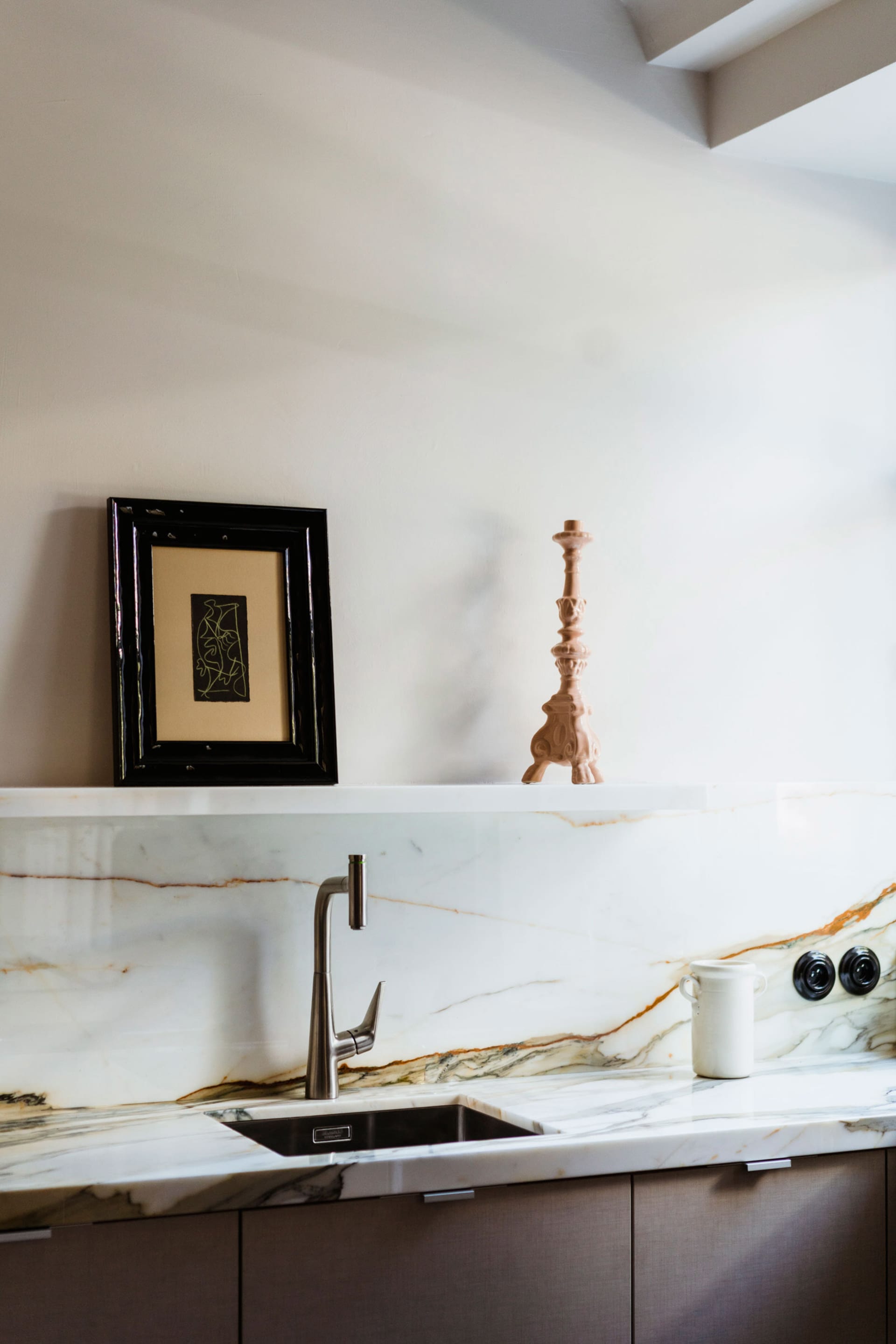 A minimalist kitchen with a white marble countertop featuring a stainless steel faucet and a white ceramic mug.