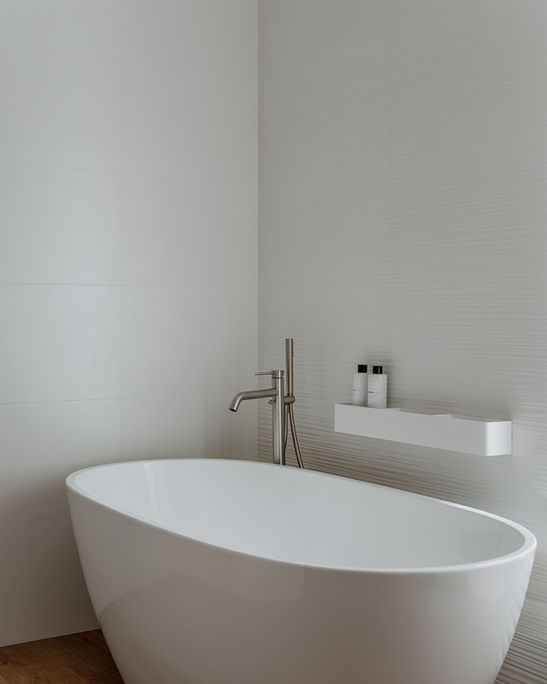 A modern bathroom with clean, white tiles and a sleek, white freestanding bathtub.