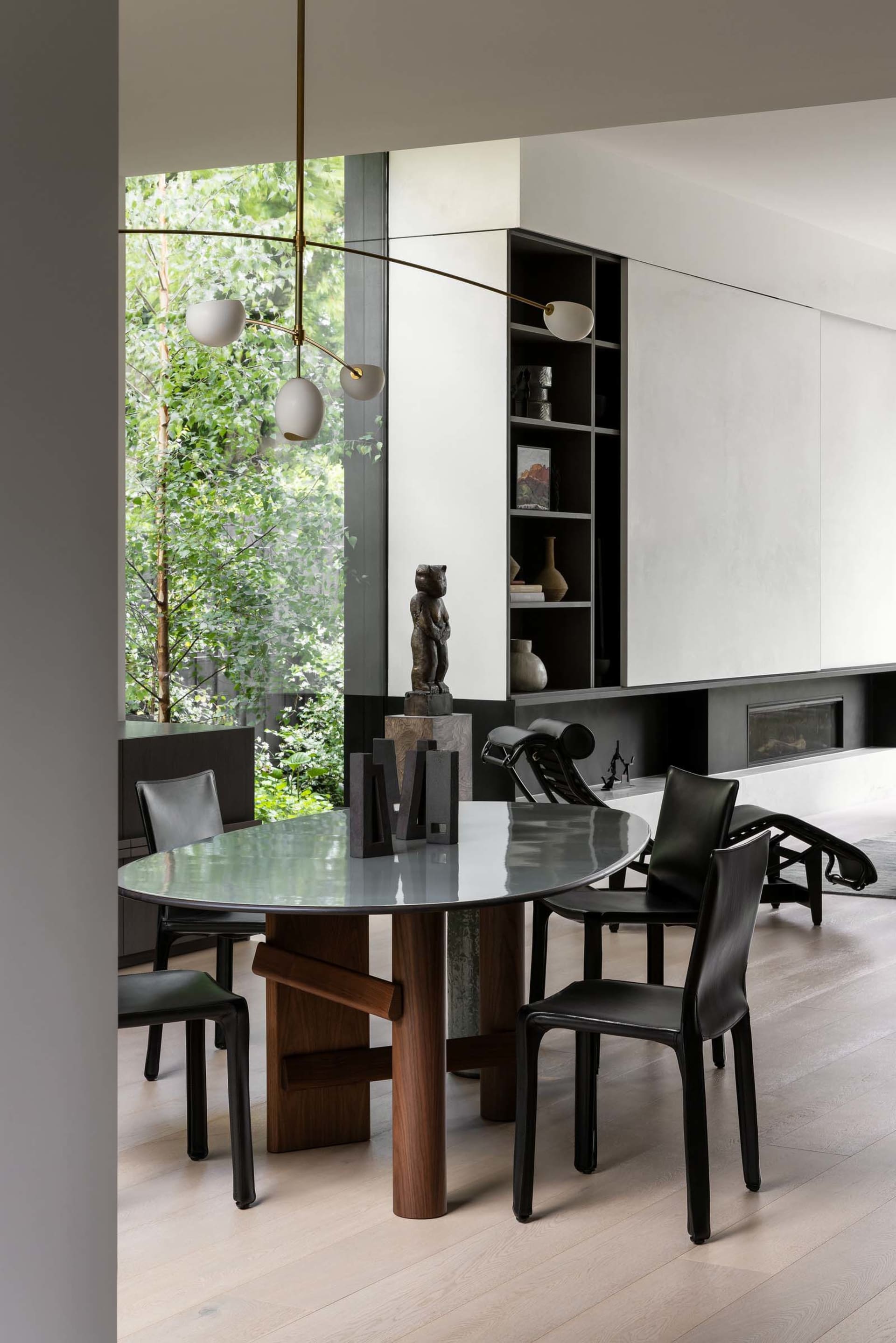 Modern dining room featuring a wooden table with a glass top, surrounded by black leather chairs and a brass pendant light.