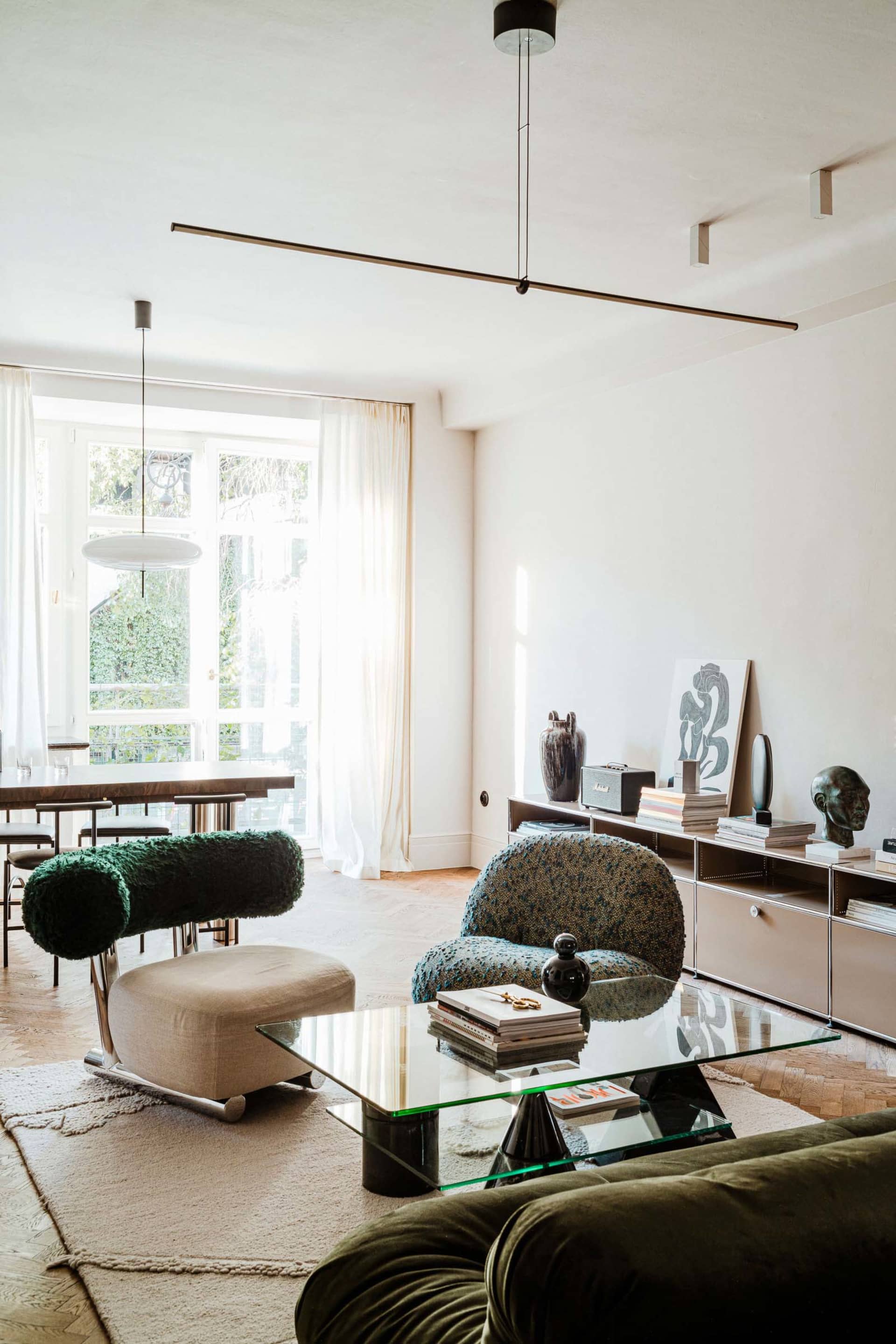 A modern living room featuring glass coffee table, fabric chairs, and wooden floor.
