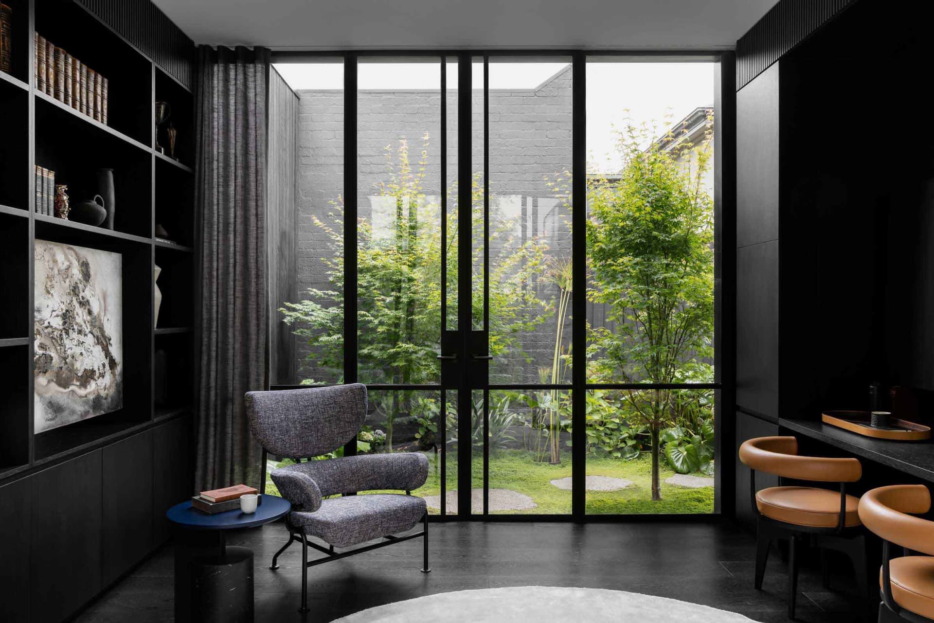 A modern living room featuring floor-to-ceiling glass walls with a view of greenery outside.