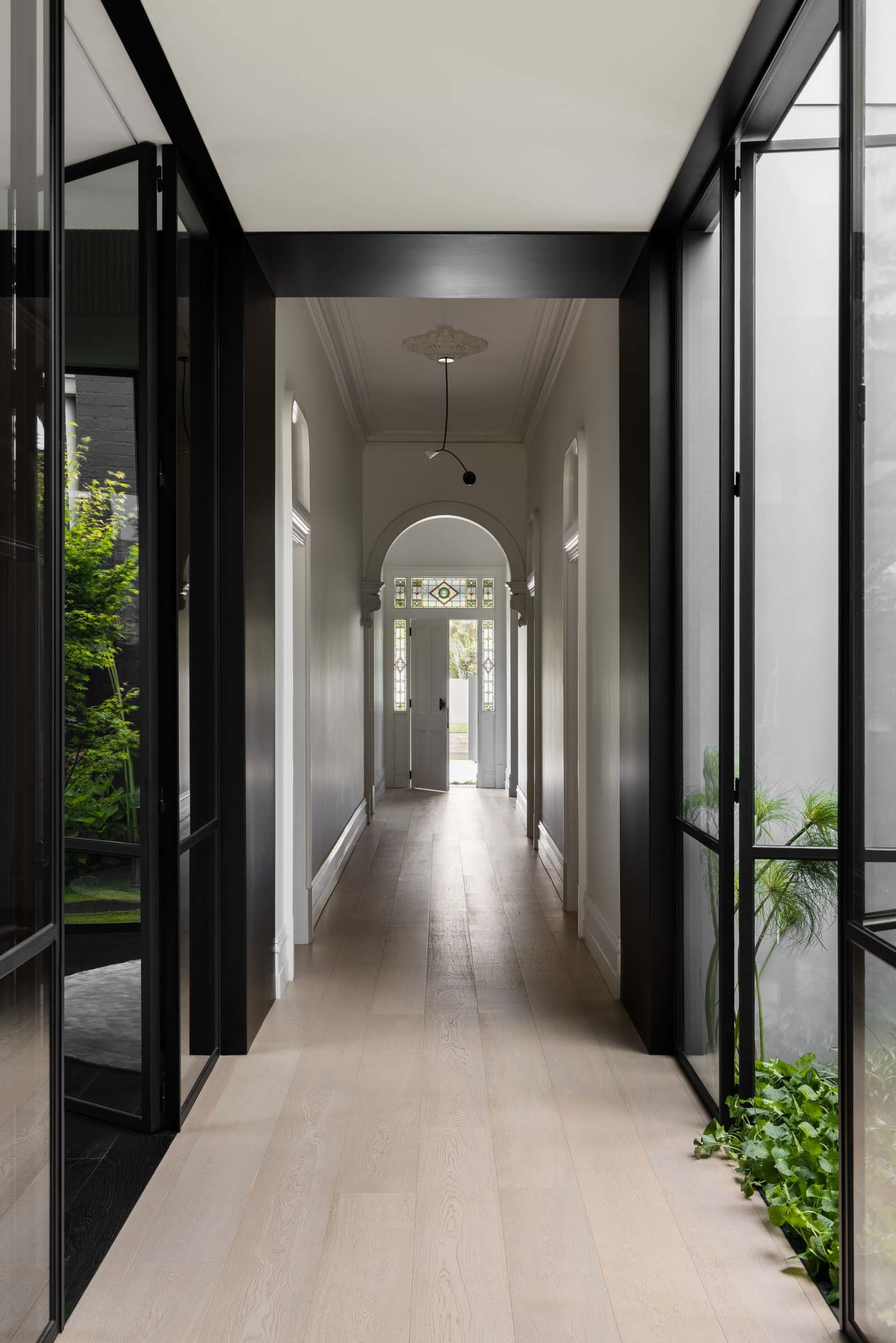 A modern minimalist hallway with light-colored wooden floors, clear glass panels, and white walls.