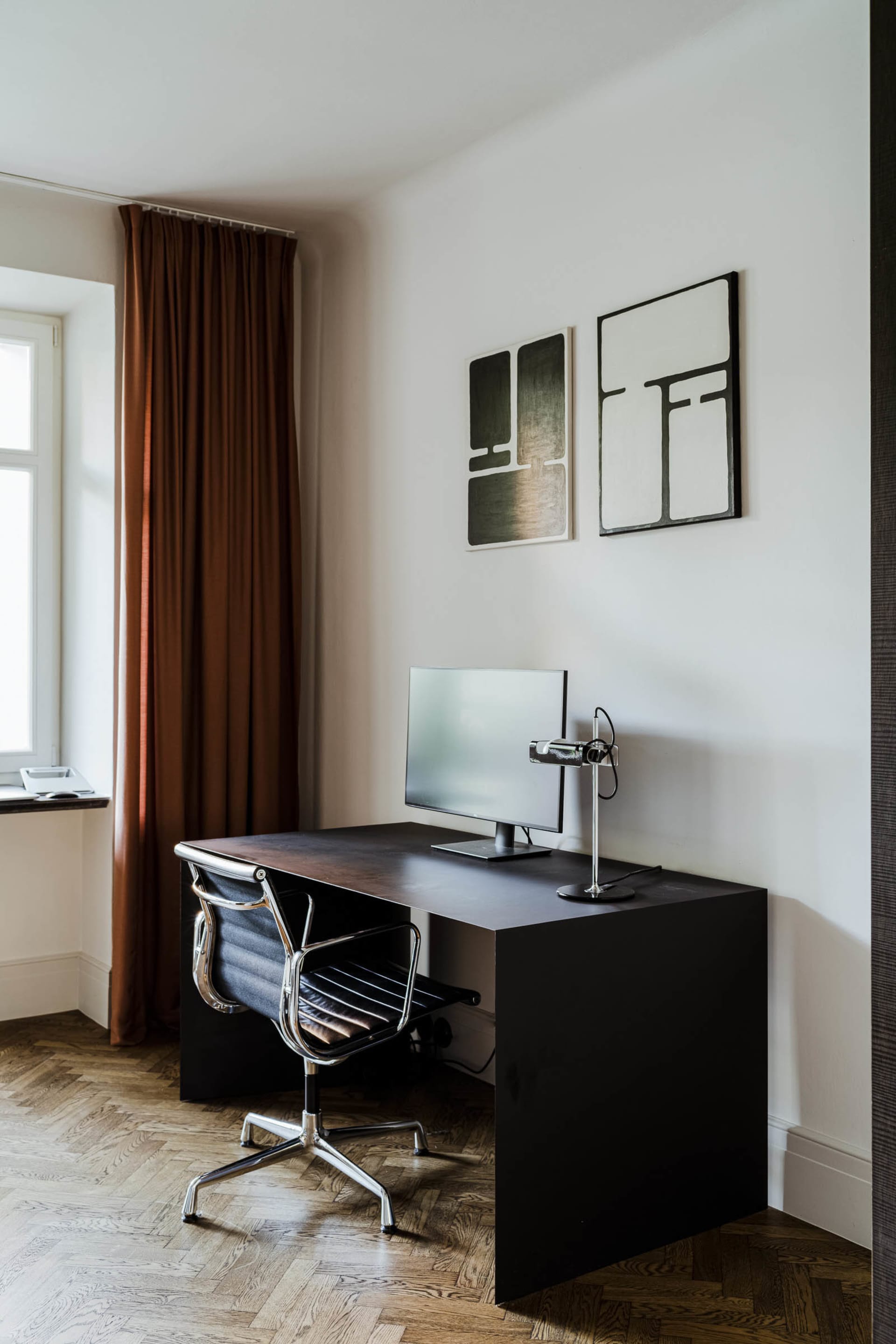 Modern minimalist home office setup with a metal desk, ergonomic chair, and framed abstract art on the wall.