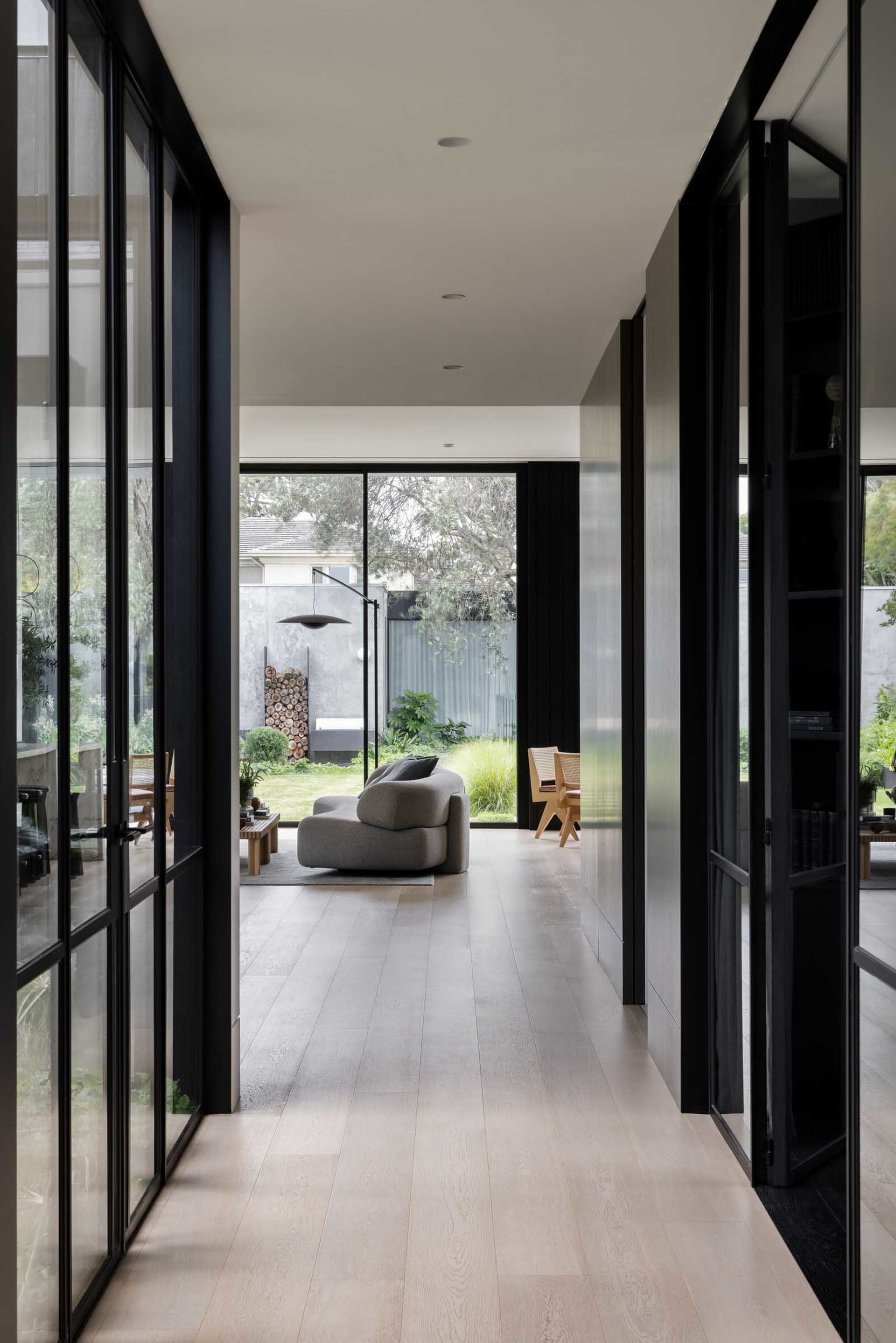Modern residential interior with hardwood flooring and large glass windows overlooking a garden.