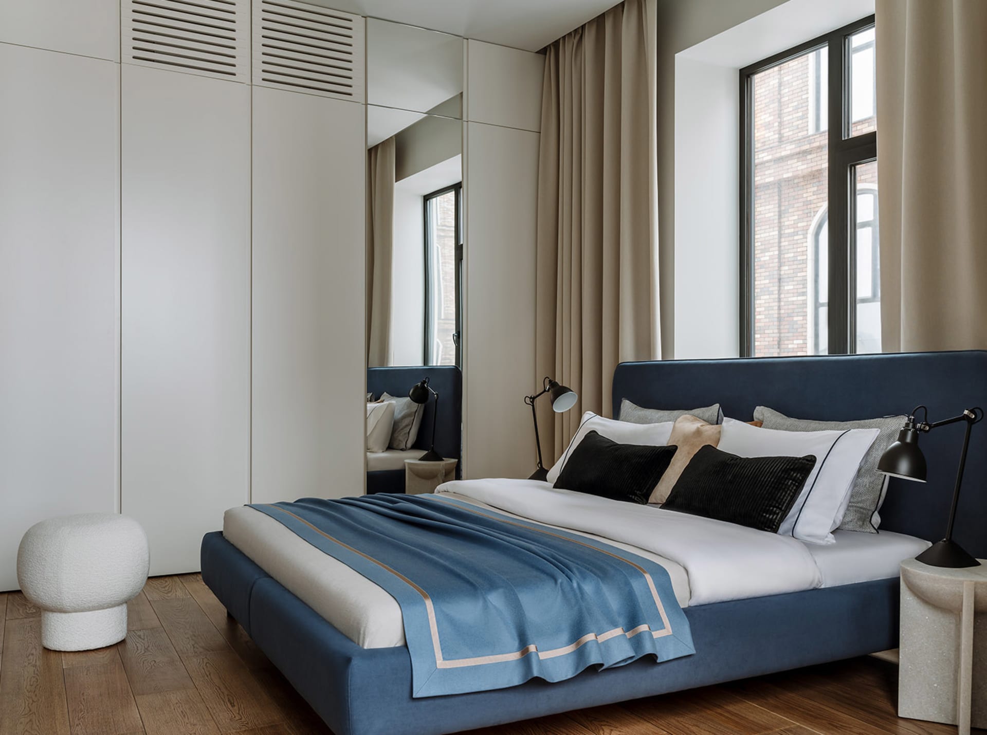 Modern minimalist bedroom with a blue upholstered bed, white linens, and black lamps.