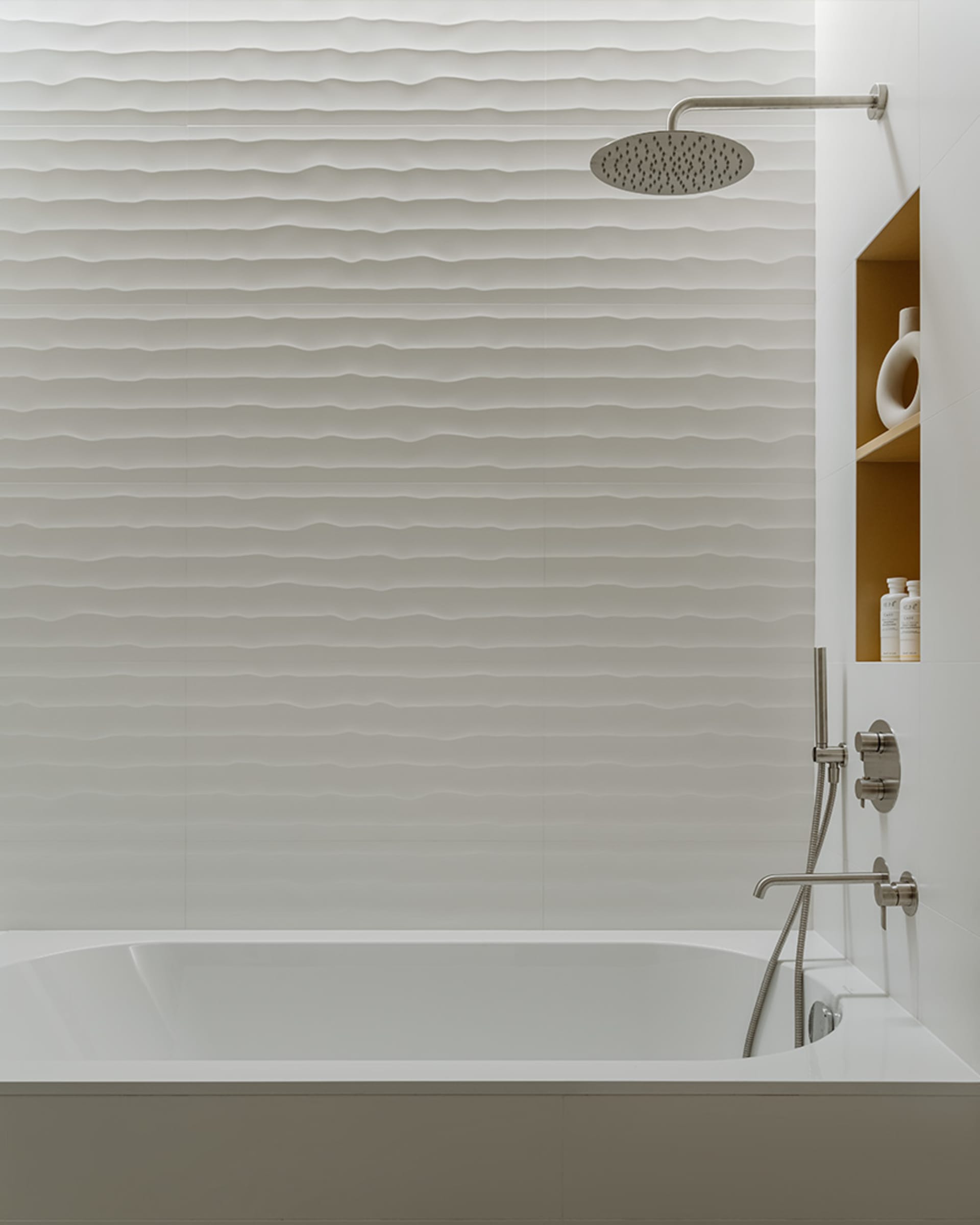 A modern, minimalist bathroom with textured white tiles covering the walls and ceiling, and a sleek, clean bathtub design.