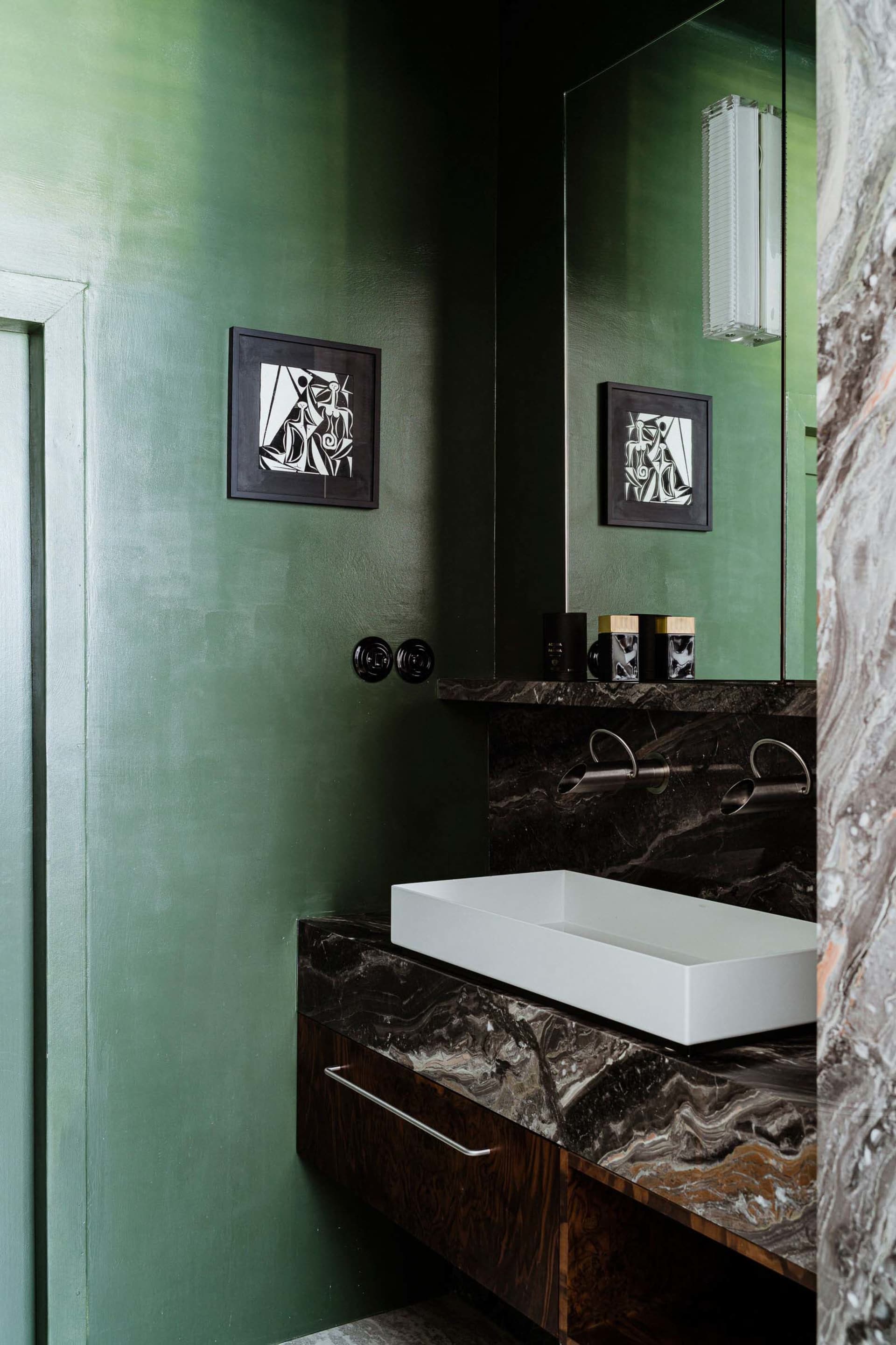 Modern bathroom featuring a white rectangular sink on a dark marble counter, with green walls and framed artwork.