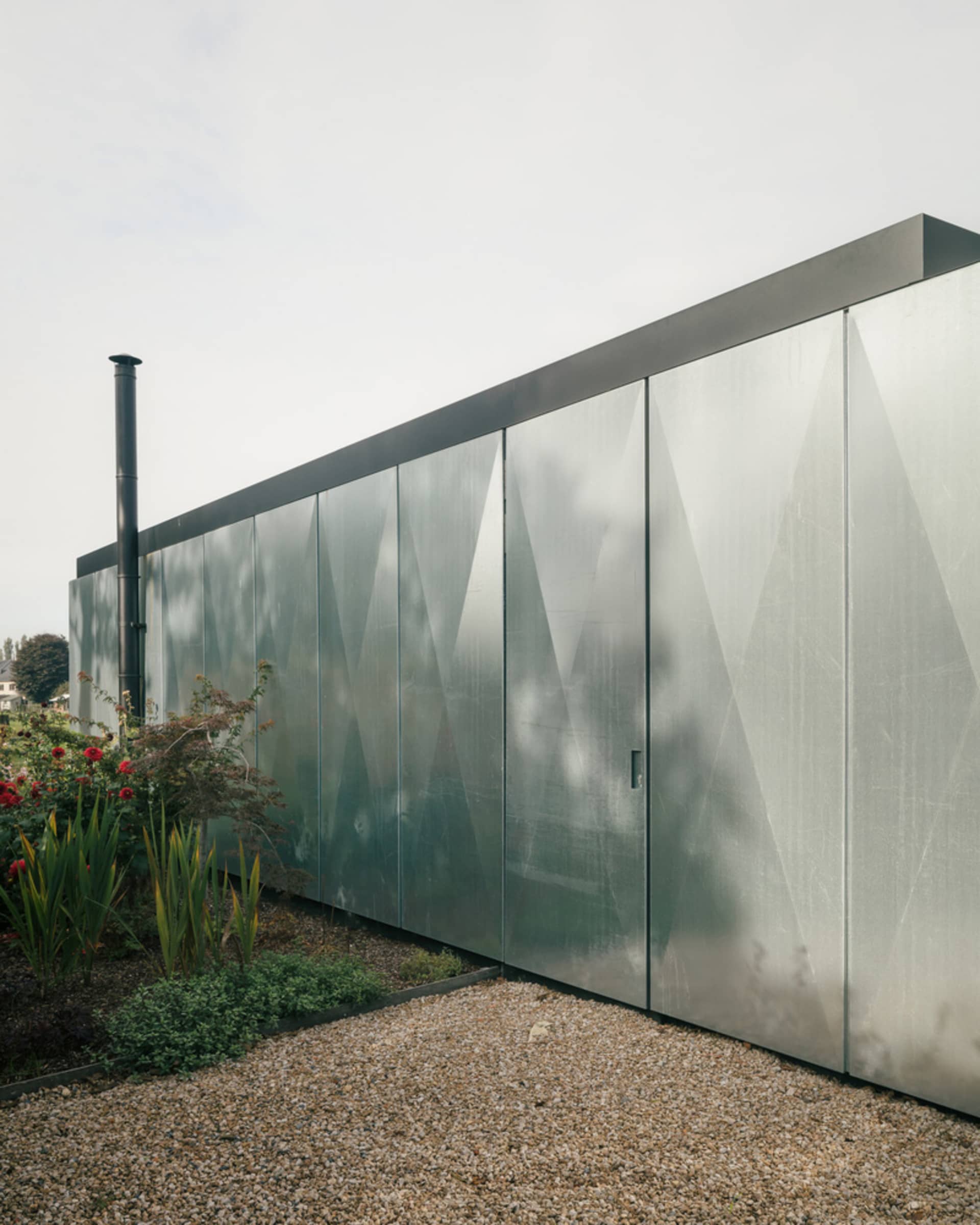 A modern exterior house with a metallic facade, featuring geometric patterns and a chimney.