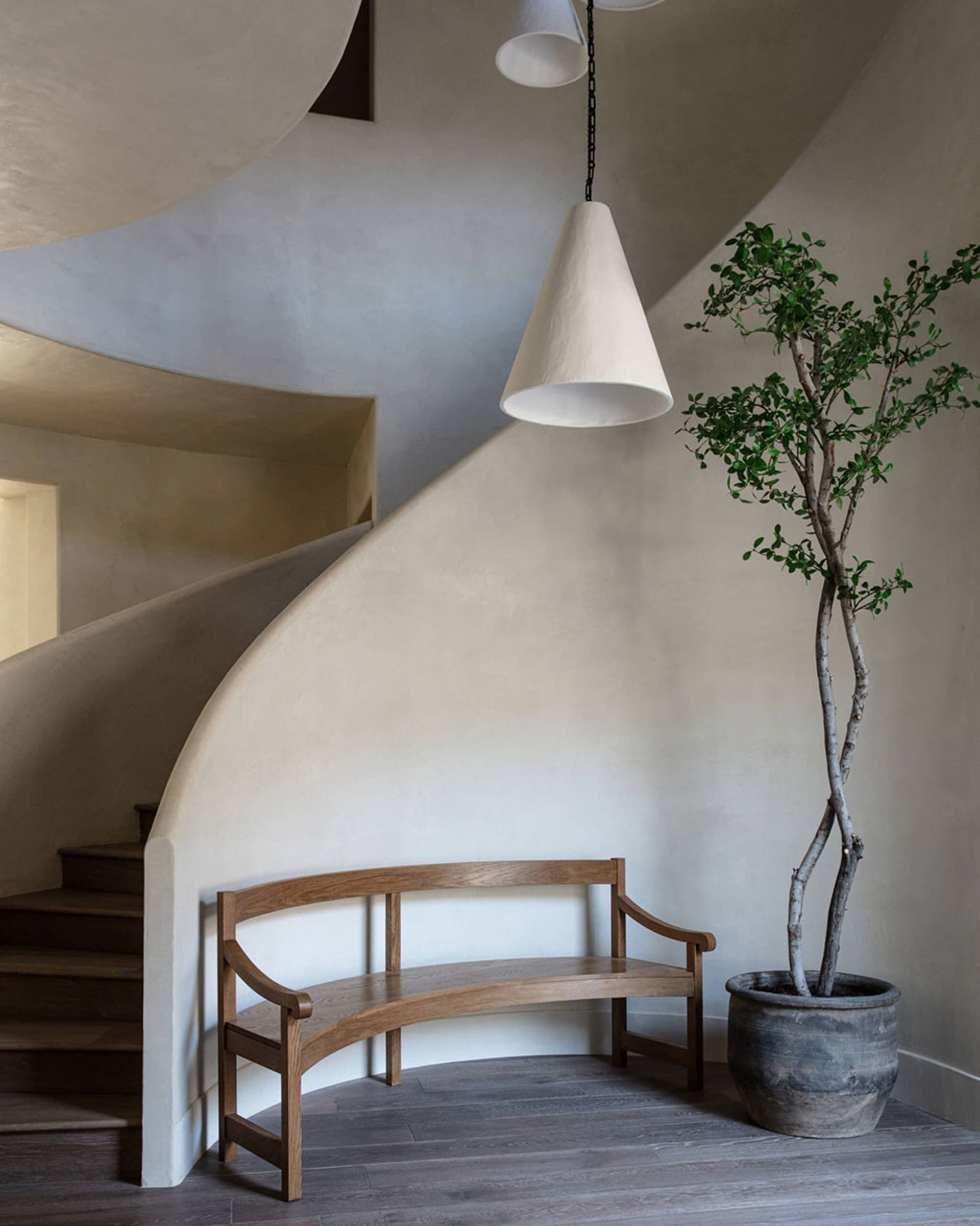 A modern minimalist living room with a wooden bench, a potted plant, and a spiral staircase.