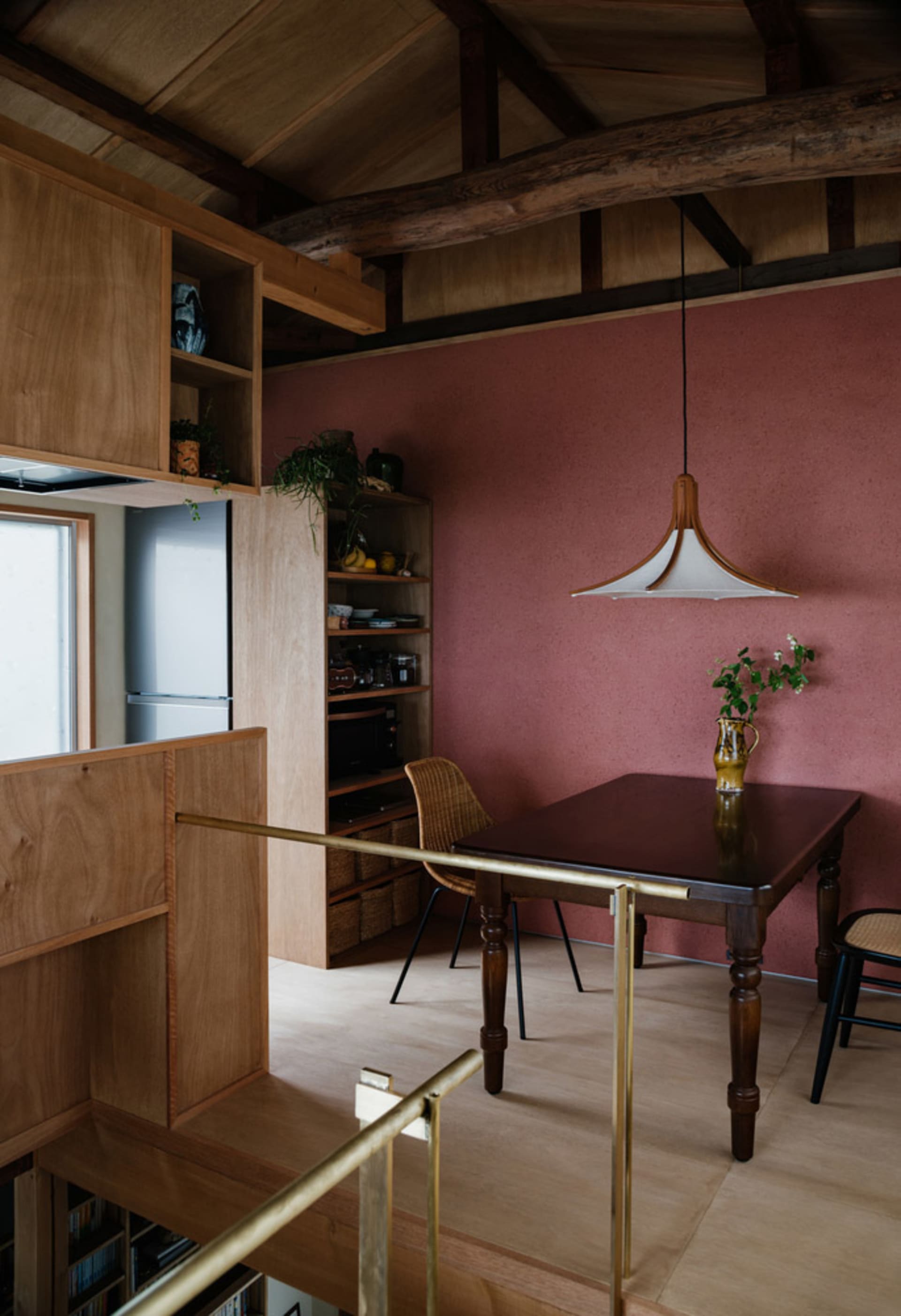 A minimalist kitchen with wooden cabinets and flooring, featuring a wooden table and chairs, and a pink wall.